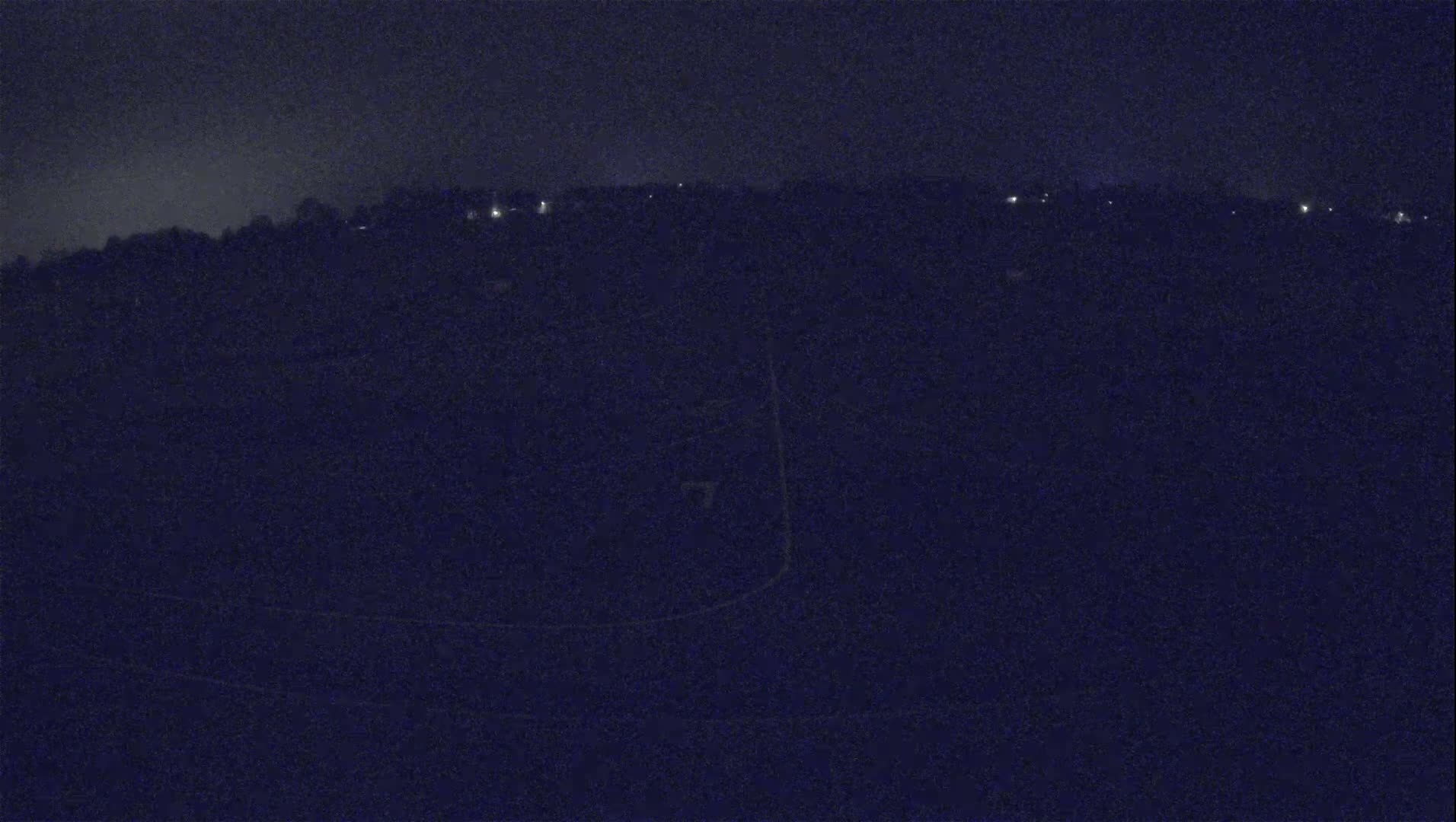 A dark, nighttime view of a landscape shows a distant line of faintly lit buildings against a dark sky.