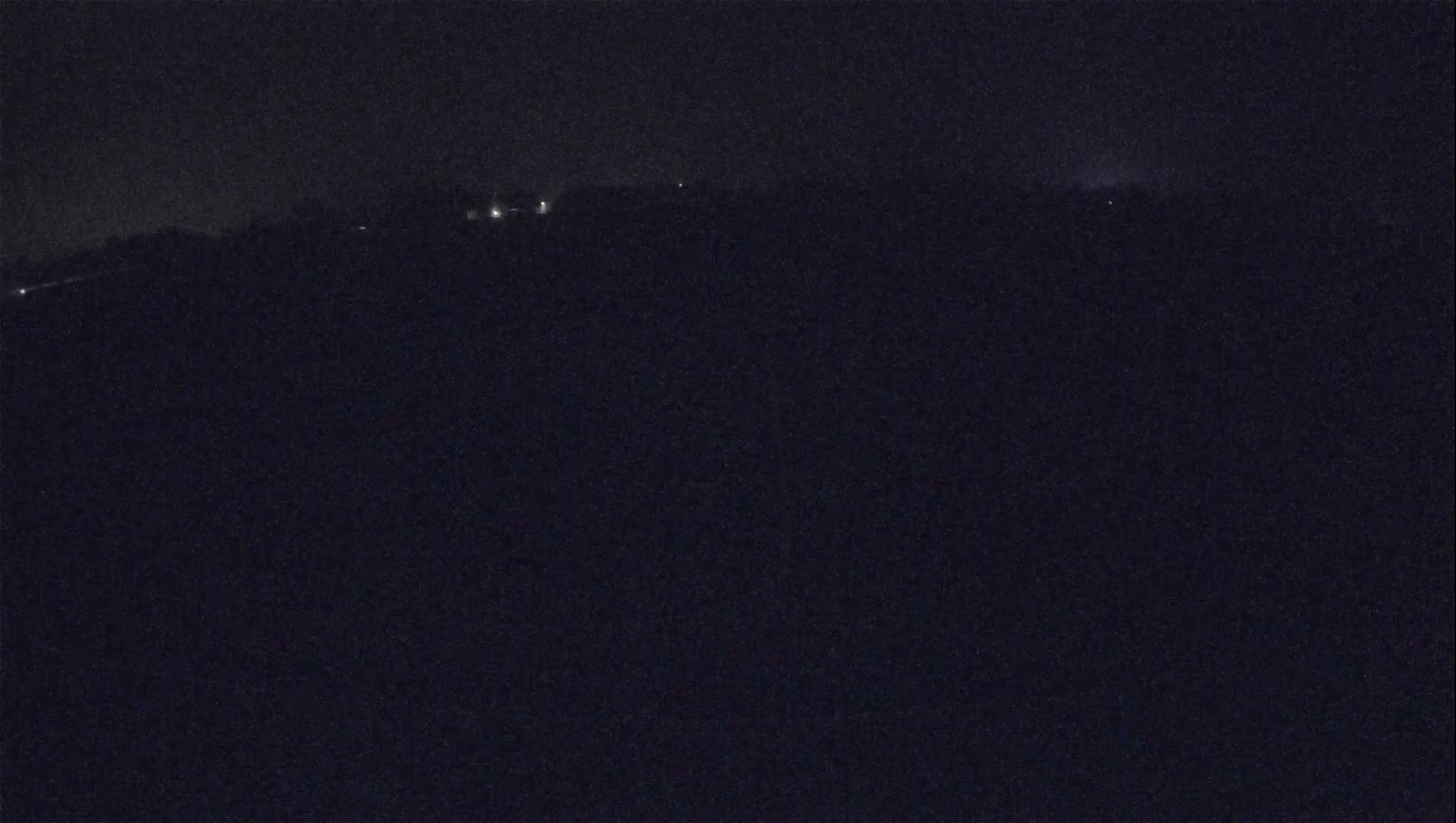 A dark, nighttime landscape shows a distant line of faint lights against a mostly black sky.