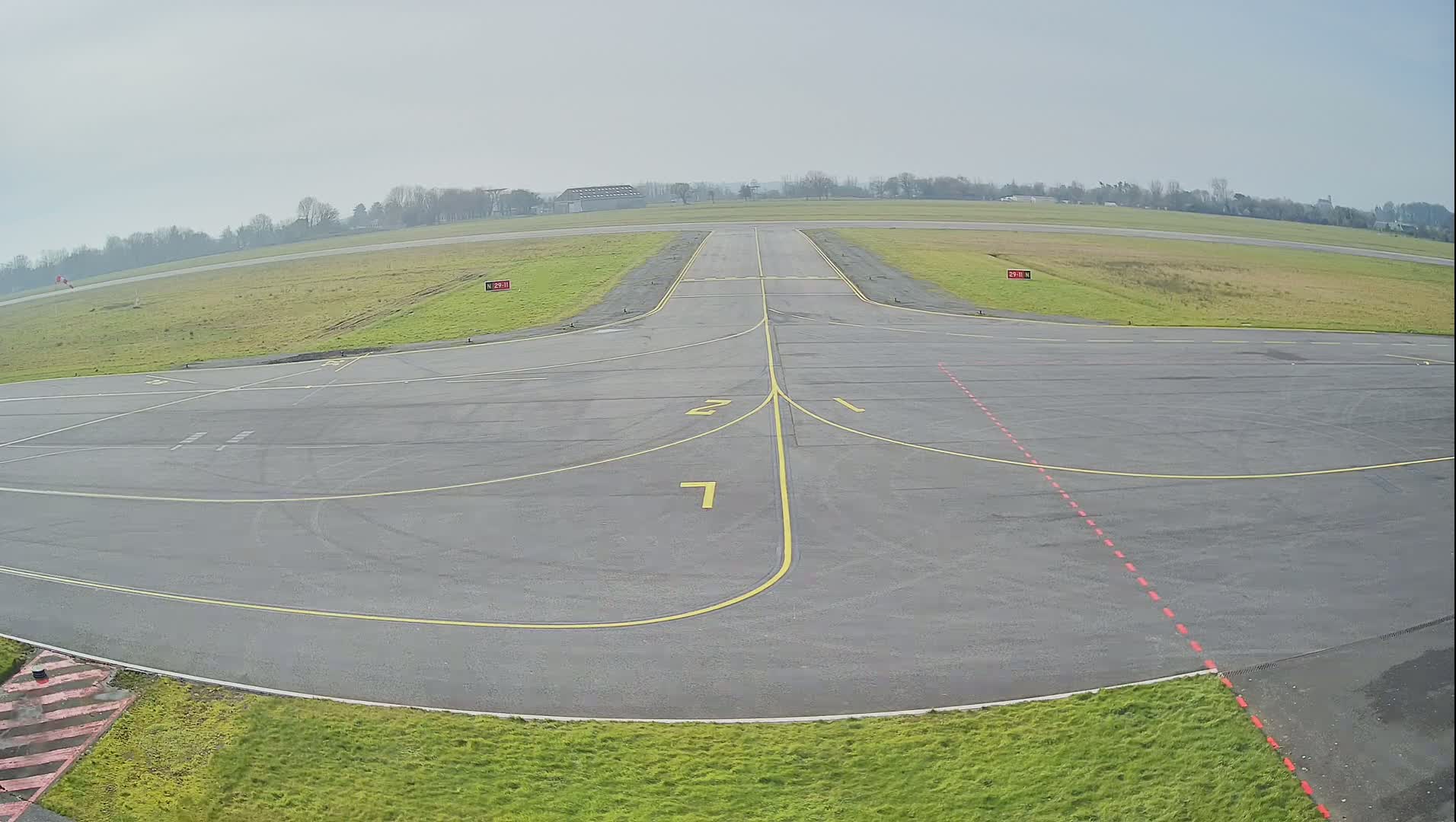 A mostly empty airport tarmac with a runway and taxiway markings is visible under a hazy sky.