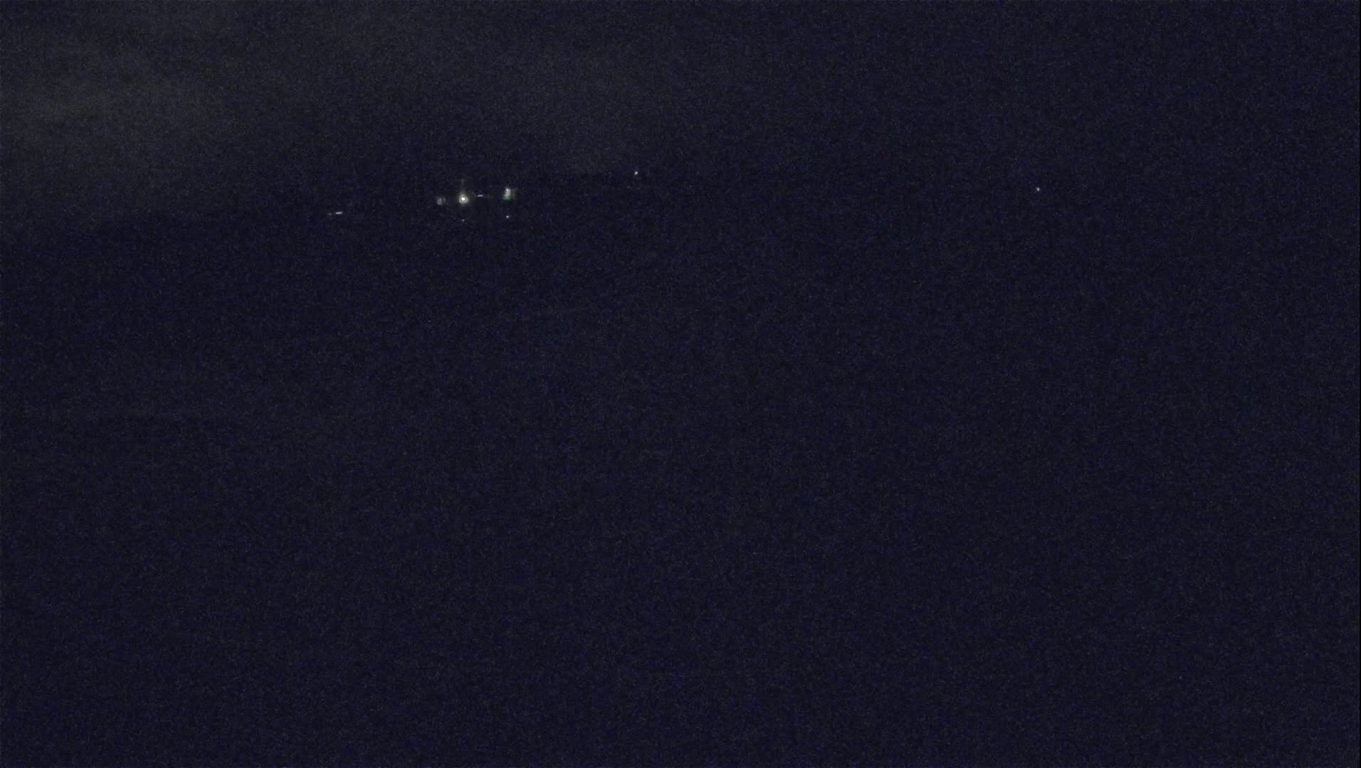 A dark, nighttime scene shows a few faint lights in the distance under a cloudy sky.