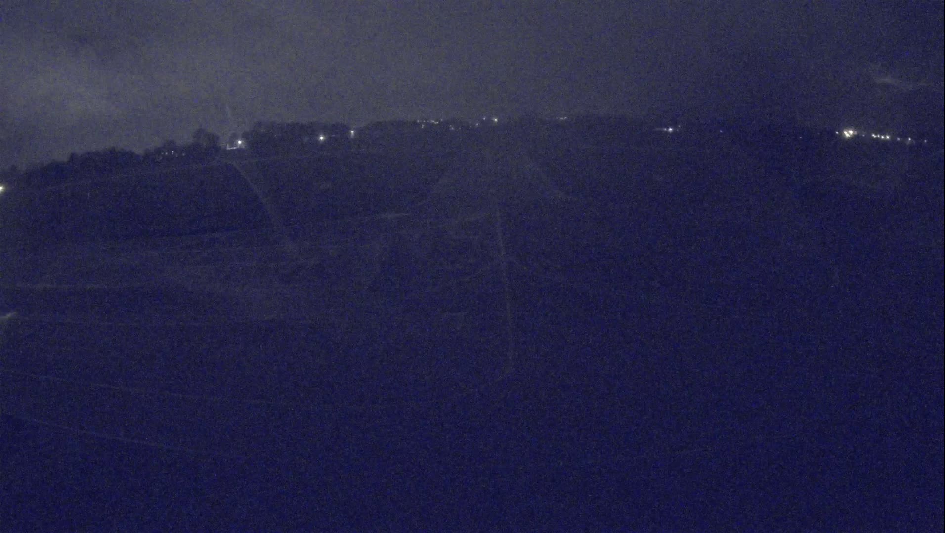 A nighttime, possibly snowy, long shot of a dark landscape with sparsely distributed lights in the distance.