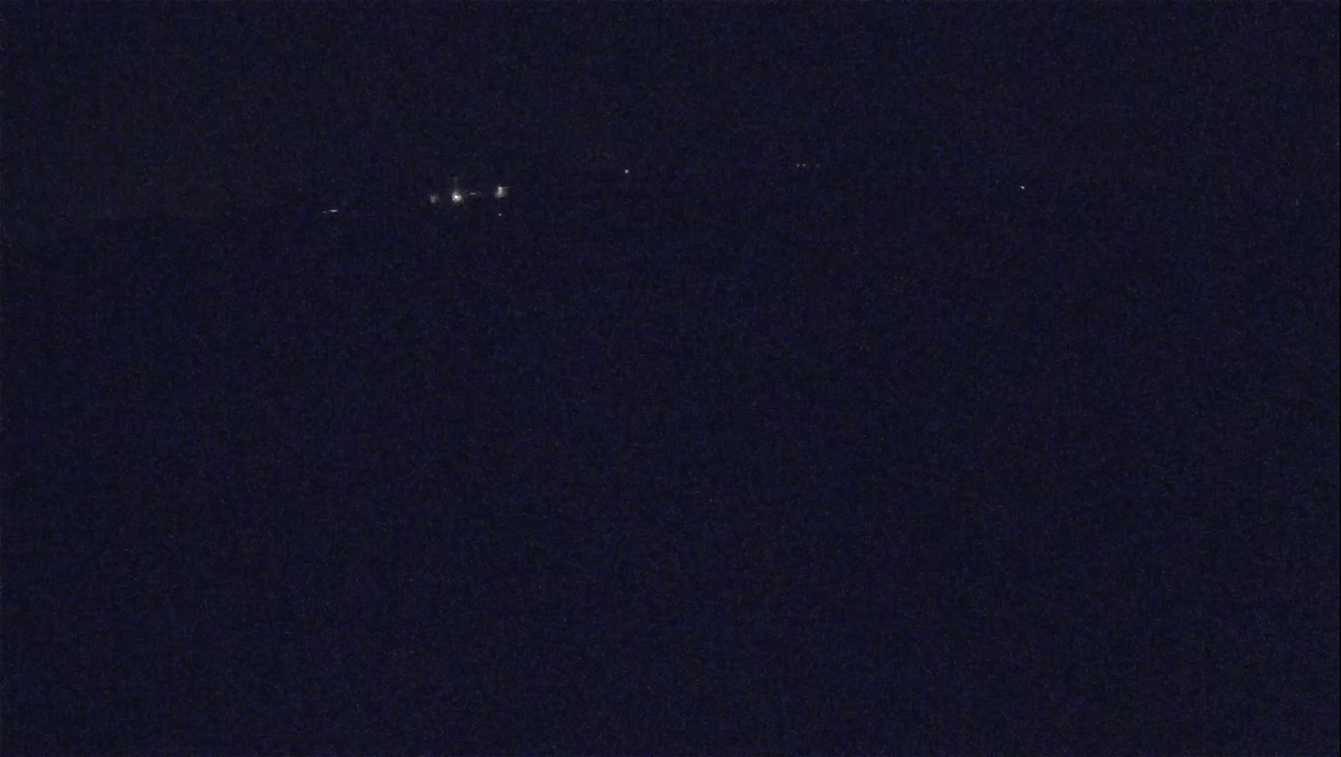 A dark, nighttime scene shows a few faint lights in the distance.