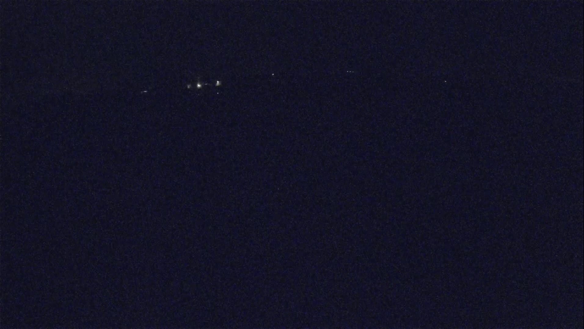 A dark, nighttime scene shows a few distant lights on the horizon.