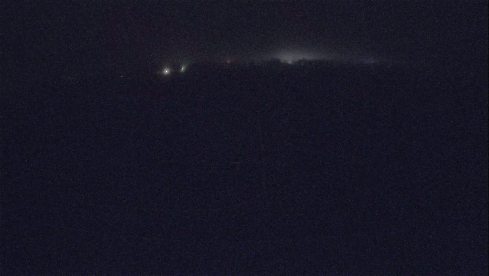 A dark, nighttime scene shows a distant line of lights obscured by haze or fog.