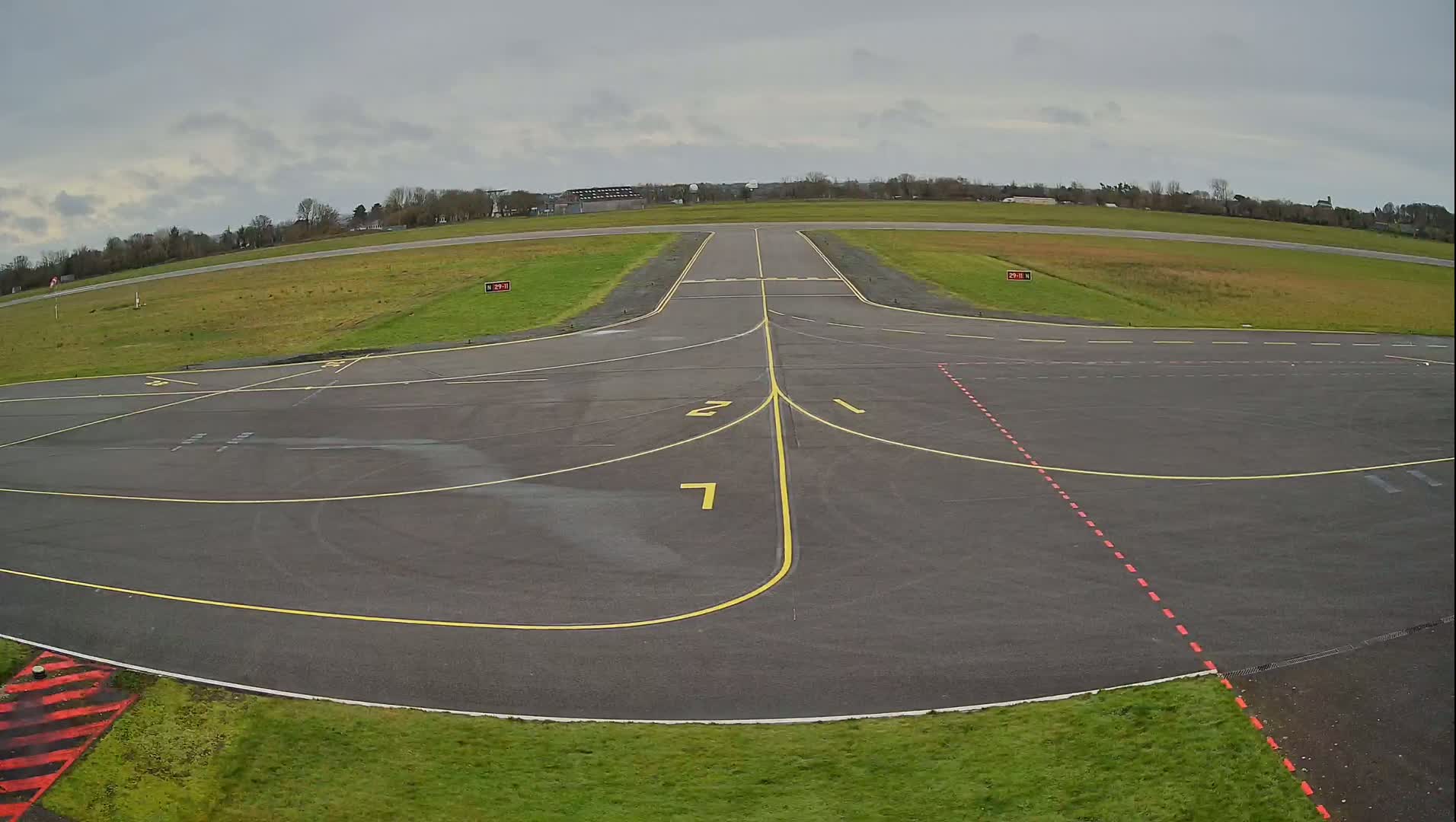 A paved airport tarmac with yellow and red markings under an overcast sky.