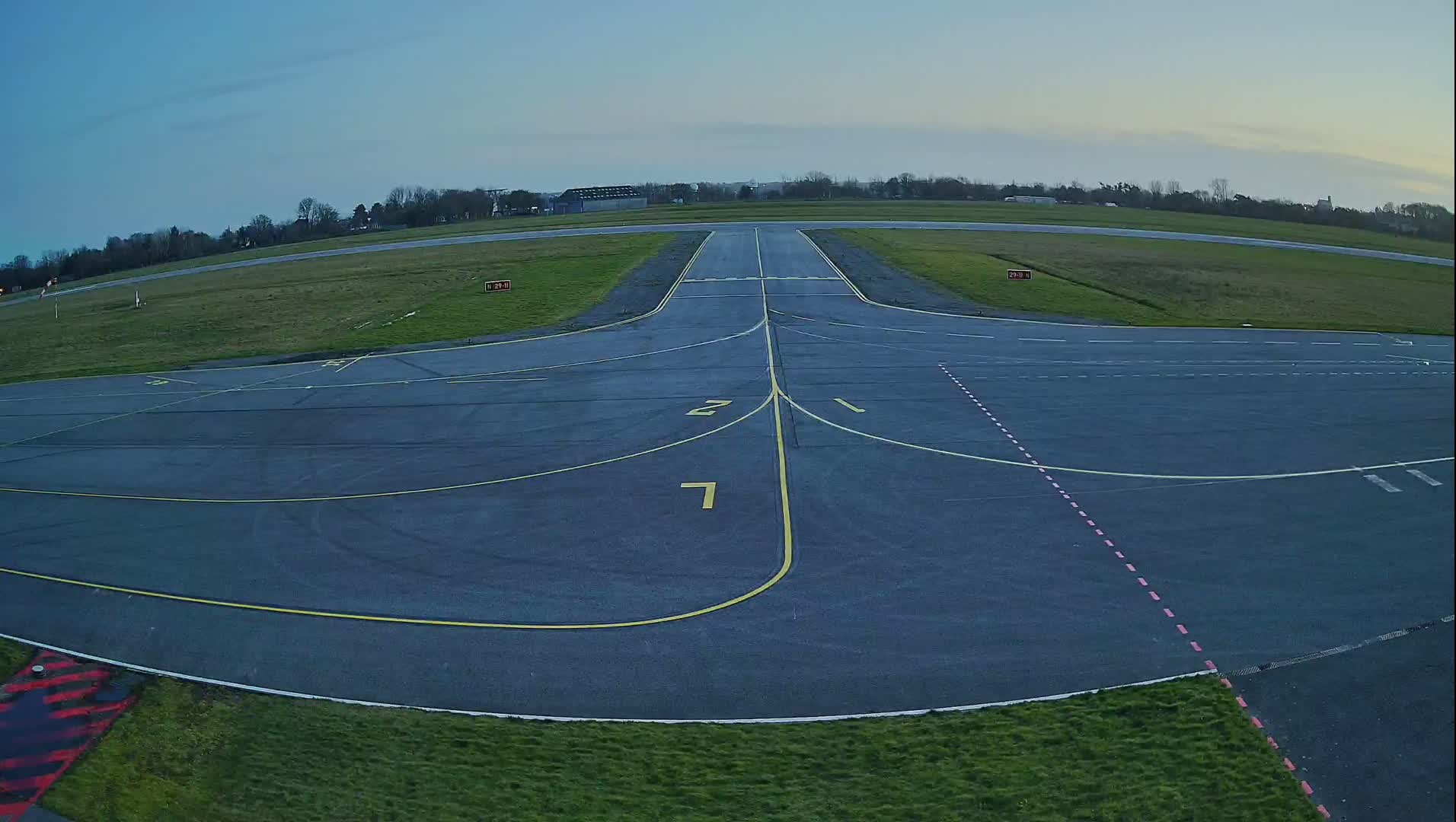 An airfield's tarmac runway and taxiways are visible under a clear, twilight sky.
