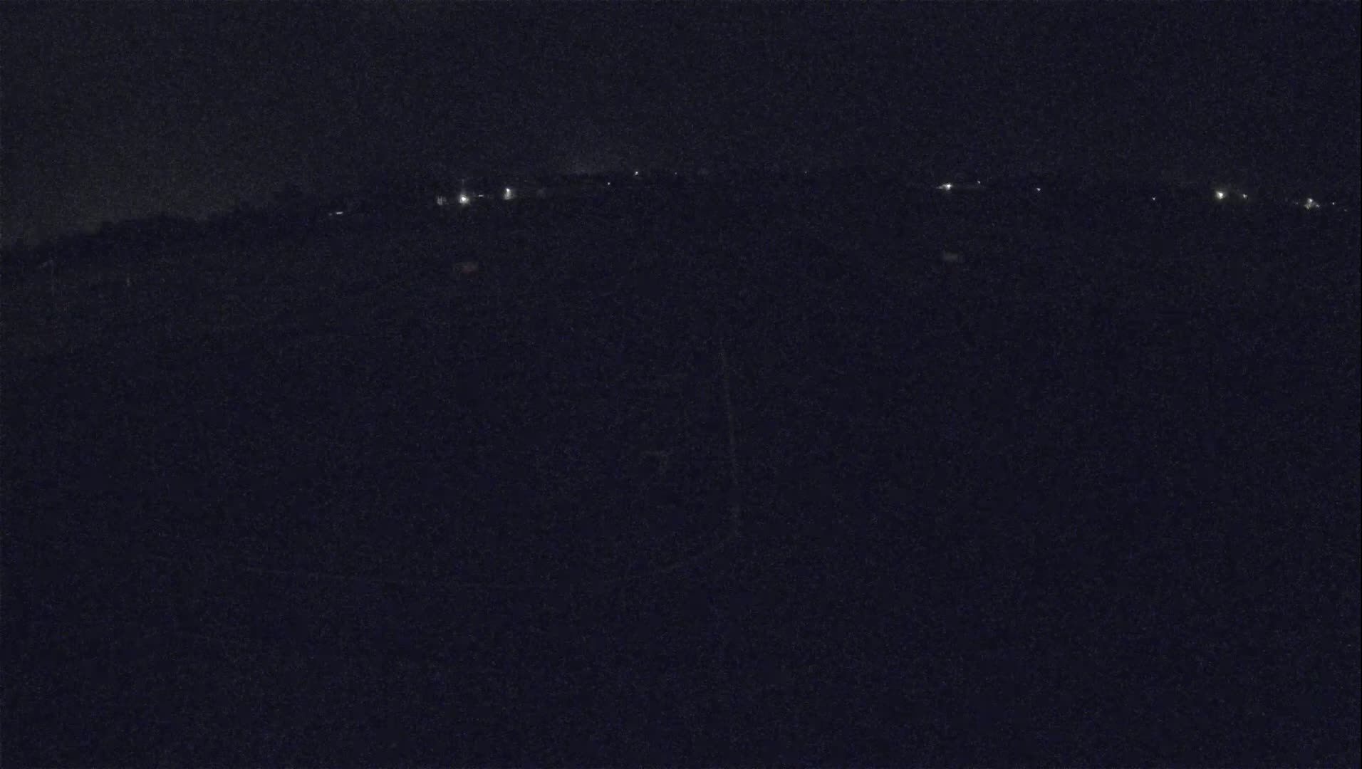 A dark, nighttime landscape shows a distant line of faint lights under a clear, black sky.