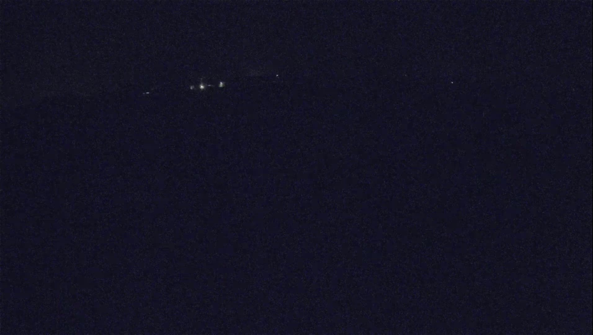 A dark, nighttime scene shows a few distant lights on a dark horizon.