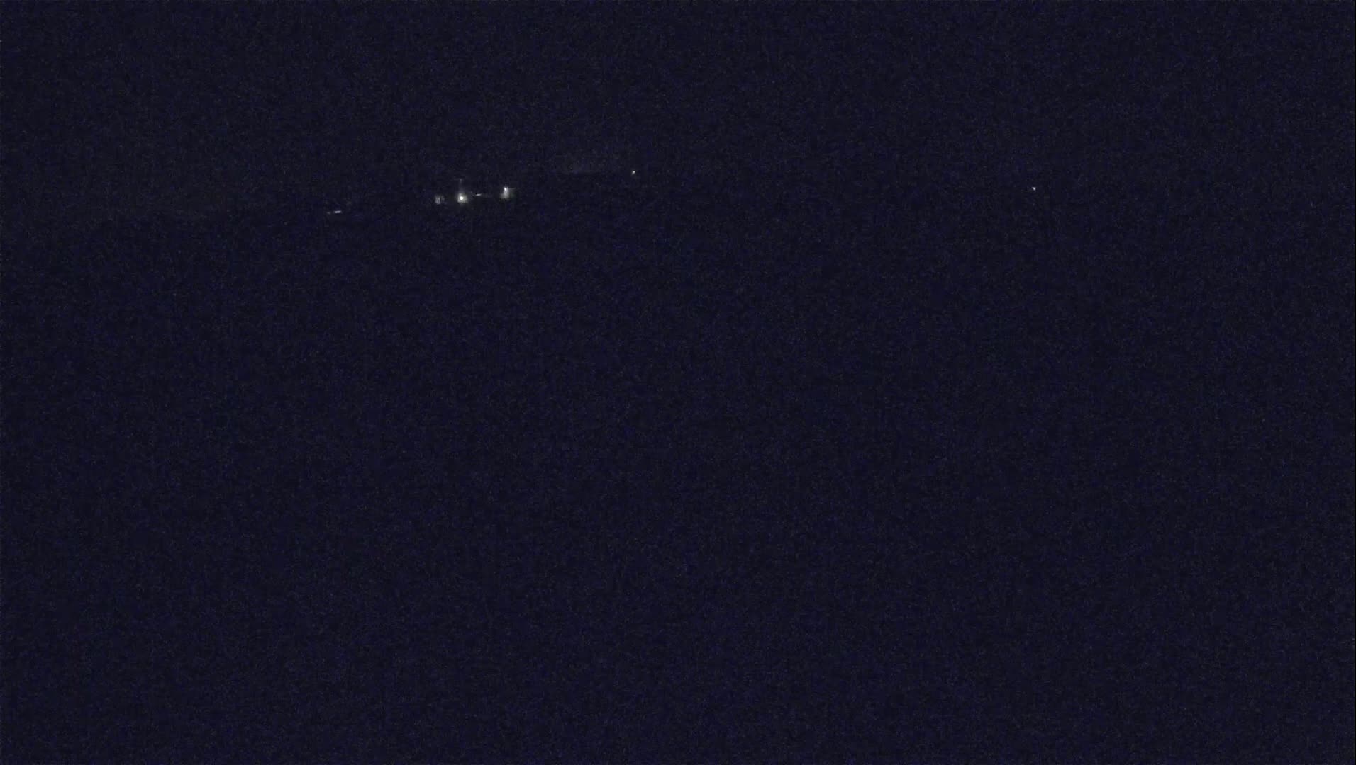 A dark, nighttime scene shows a few faint lights in the distance.