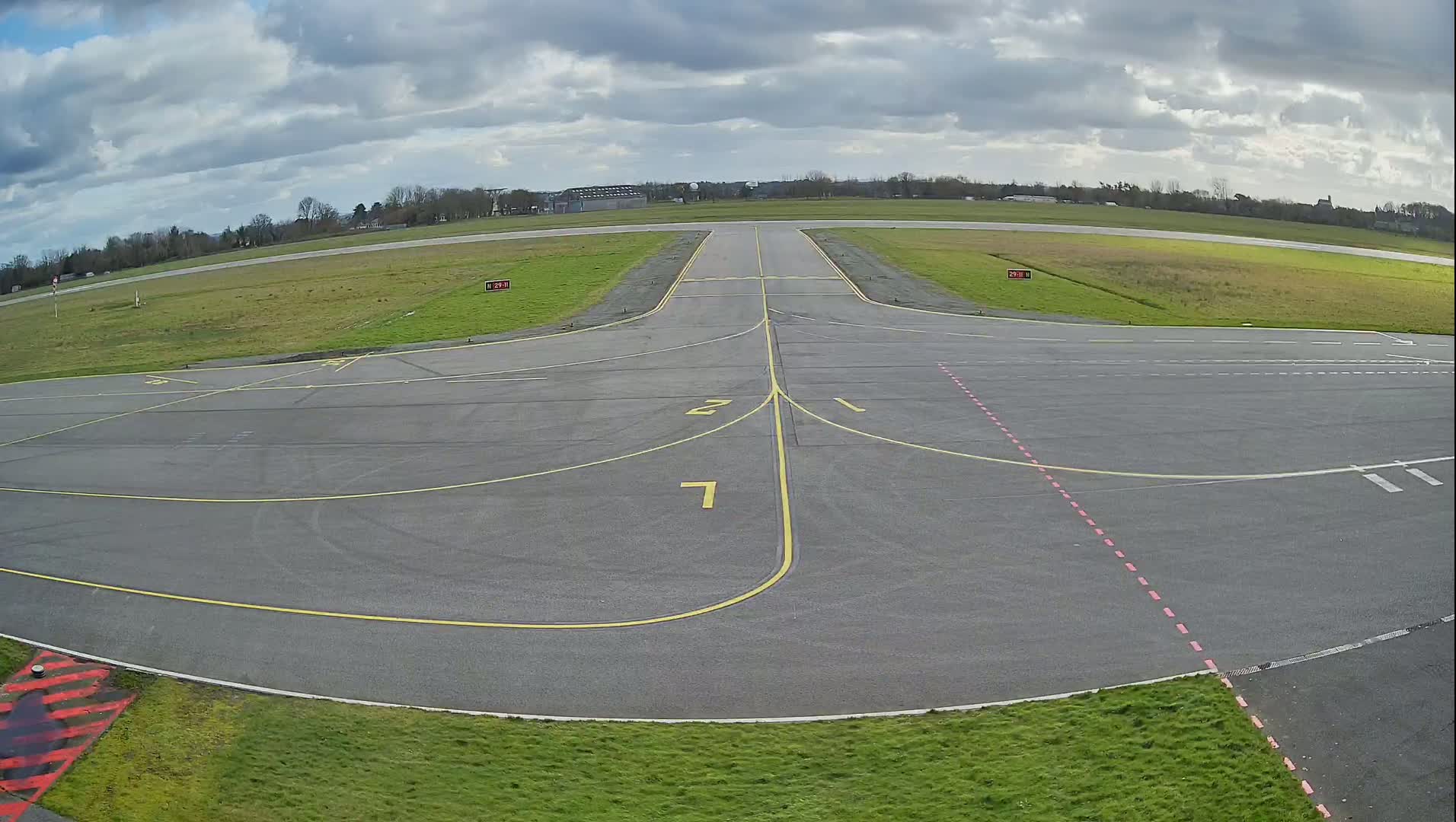 An airport tarmac with yellow and pink markings is shown under a partly cloudy sky.