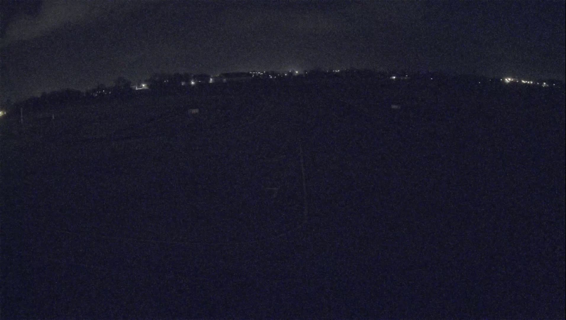 A dark, nighttime view of a field with a distant line of faint lights.