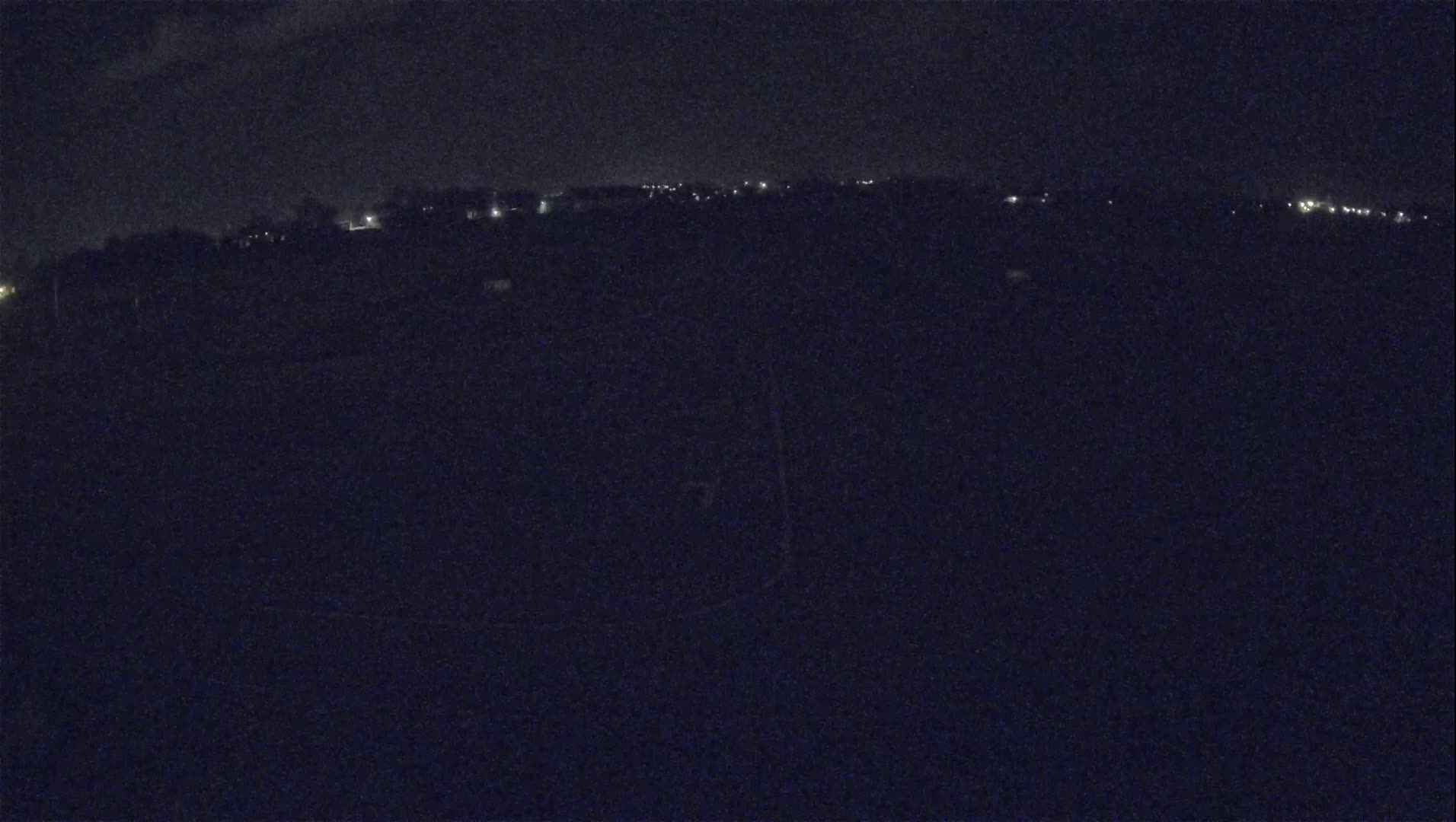 A nighttime, low-light view shows a dark landscape with a distant line of faint lights.