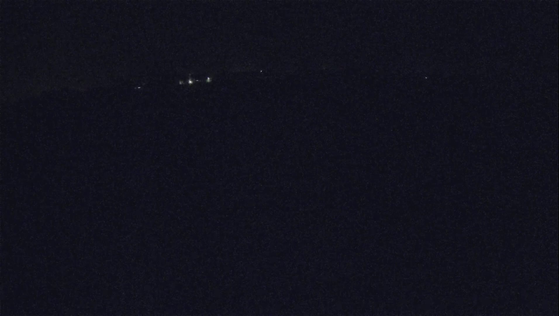 A dark, nighttime scene shows a few distant lights on a horizon.