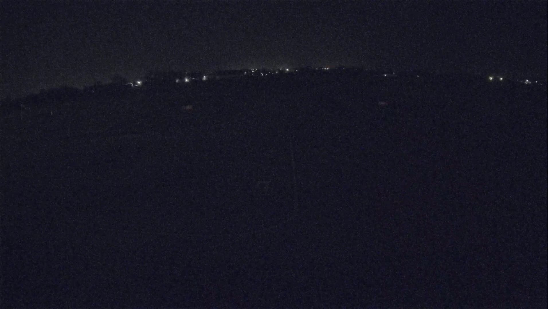 A nighttime, long-range view shows a dark landscape with a line of distant, faint lights.