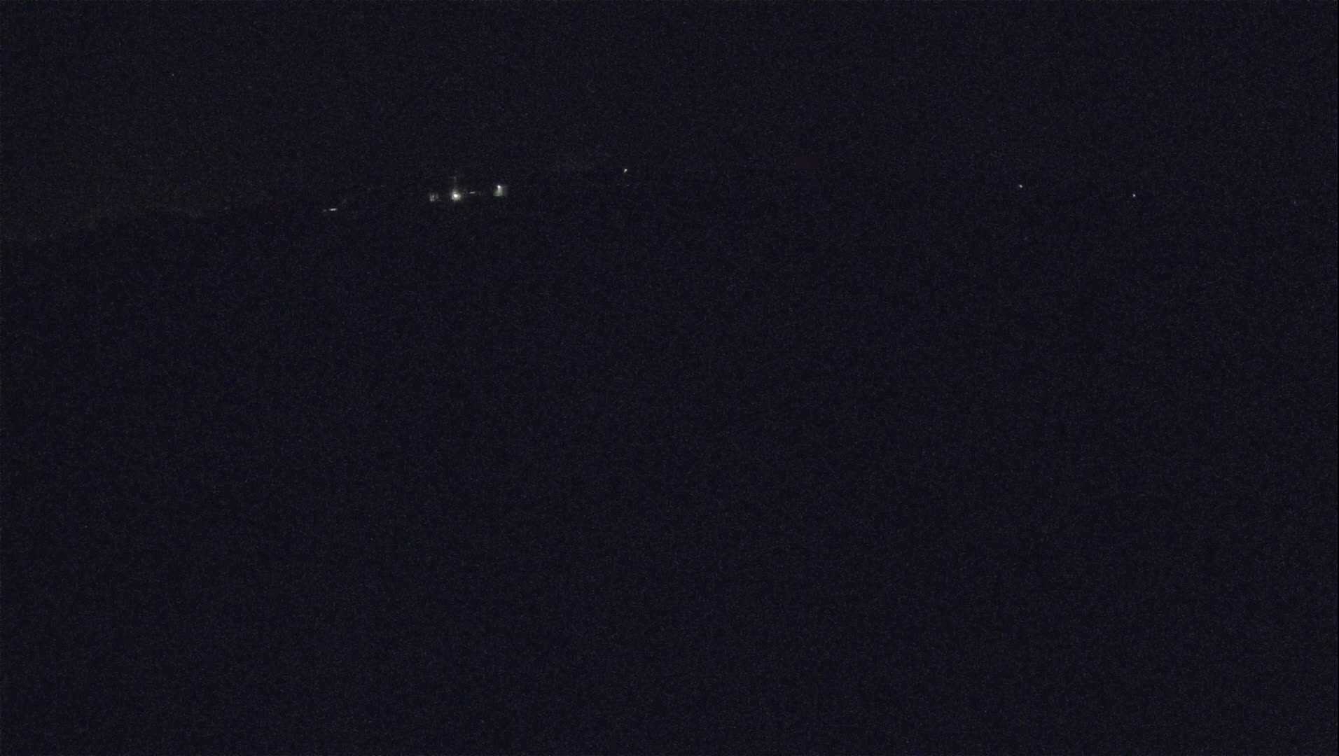 A dark, nighttime scene shows a few distant lights in the upper-middle section of the image.