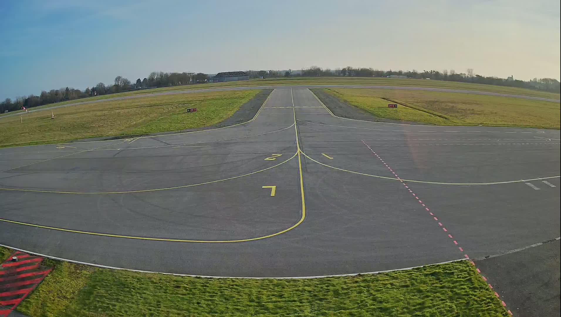 An airfield's tarmac apron and runway intersection are visible under a clear blue sky.