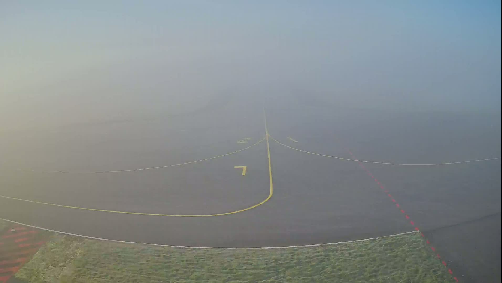 A foggy runway with yellow lines marking the taxiway is visible, surrounded by short green grass.