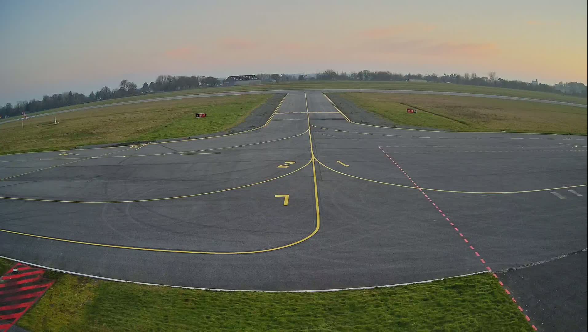 An airfield's tarmac apron and runway are visible under a twilight sky.