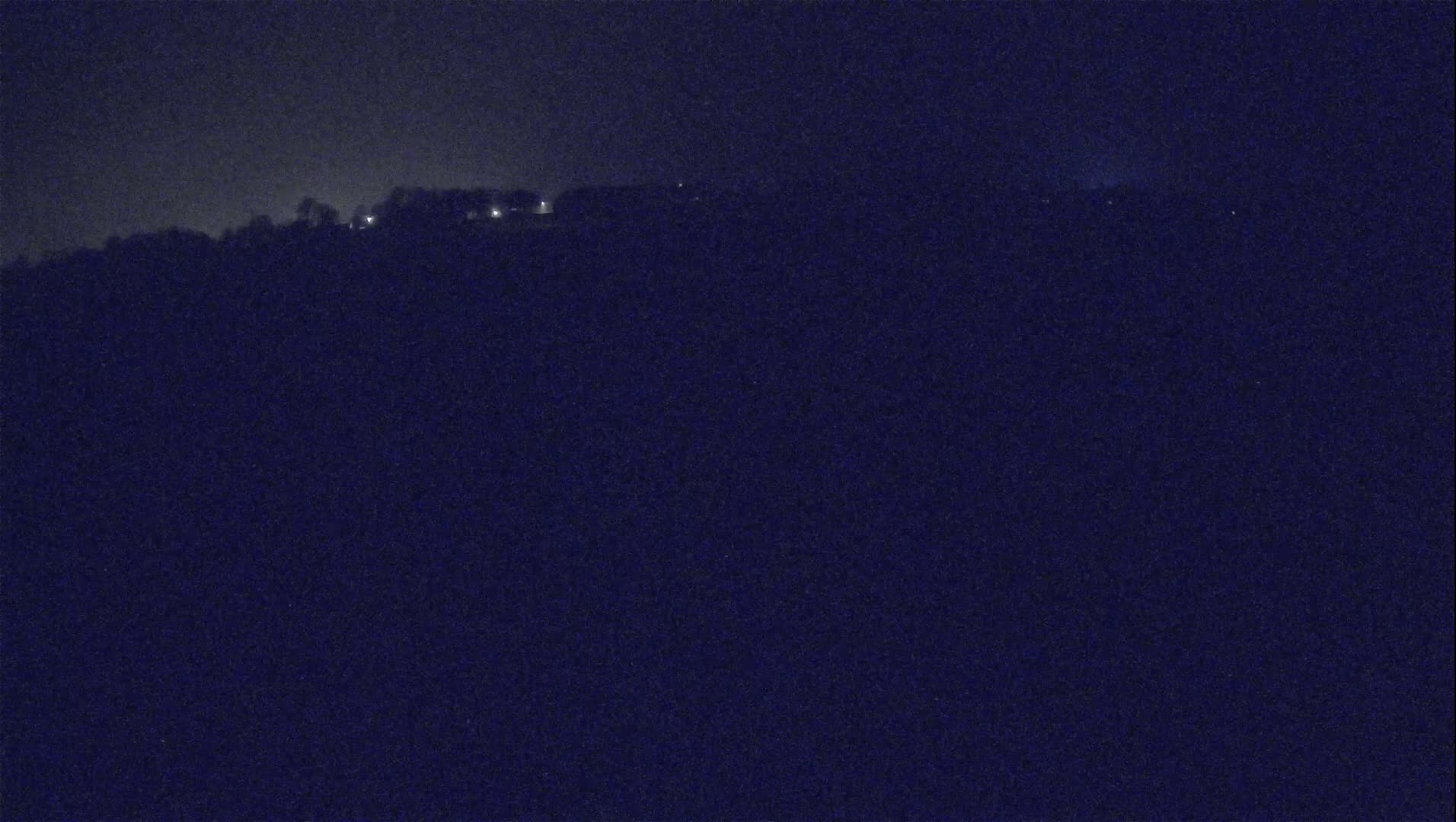 A dark, nighttime view of a hilltop with a few distant lights visible against a dark sky.