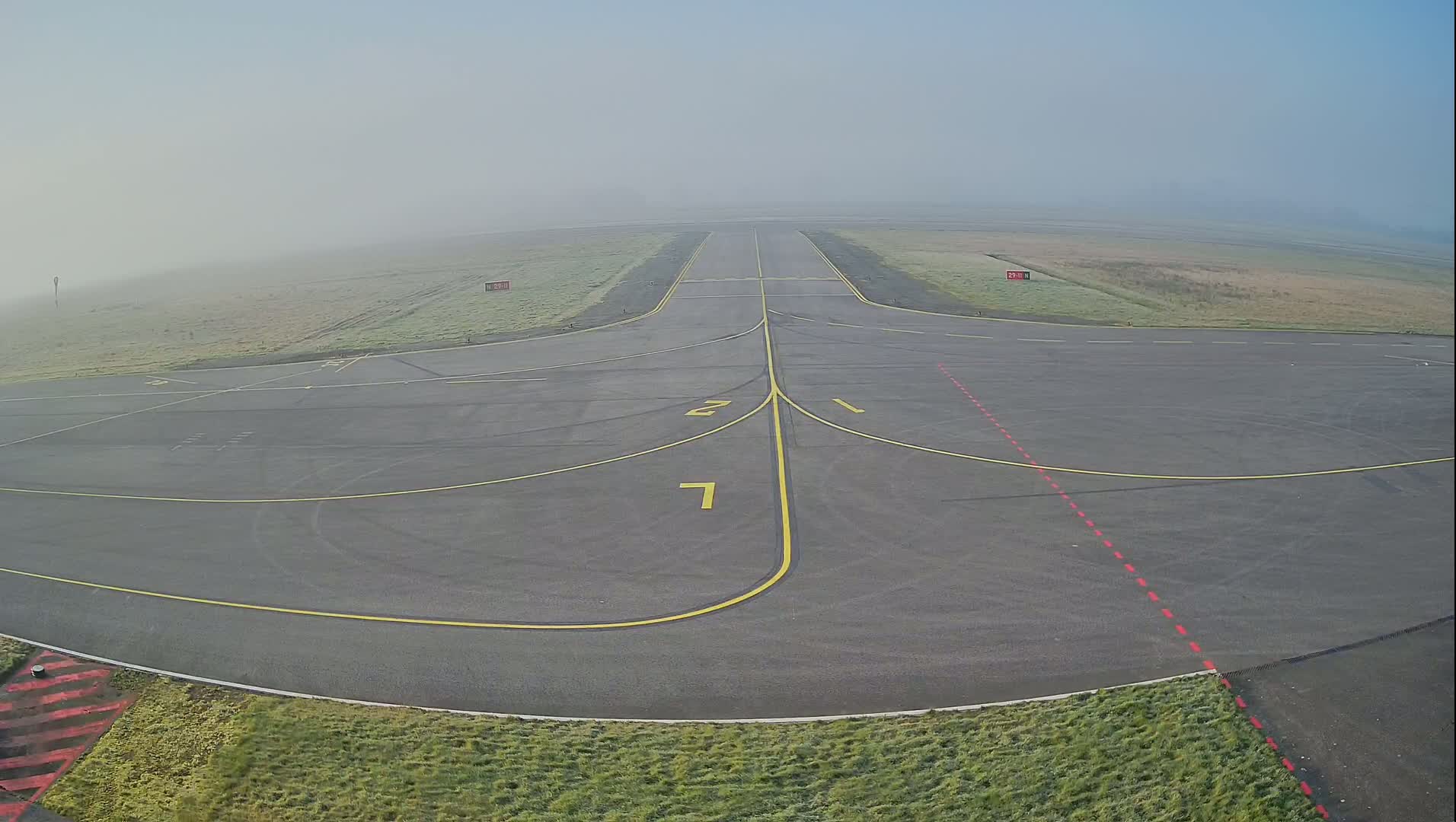 A foggy airfield runway and taxiway are visible, marked with yellow lines and numbers.