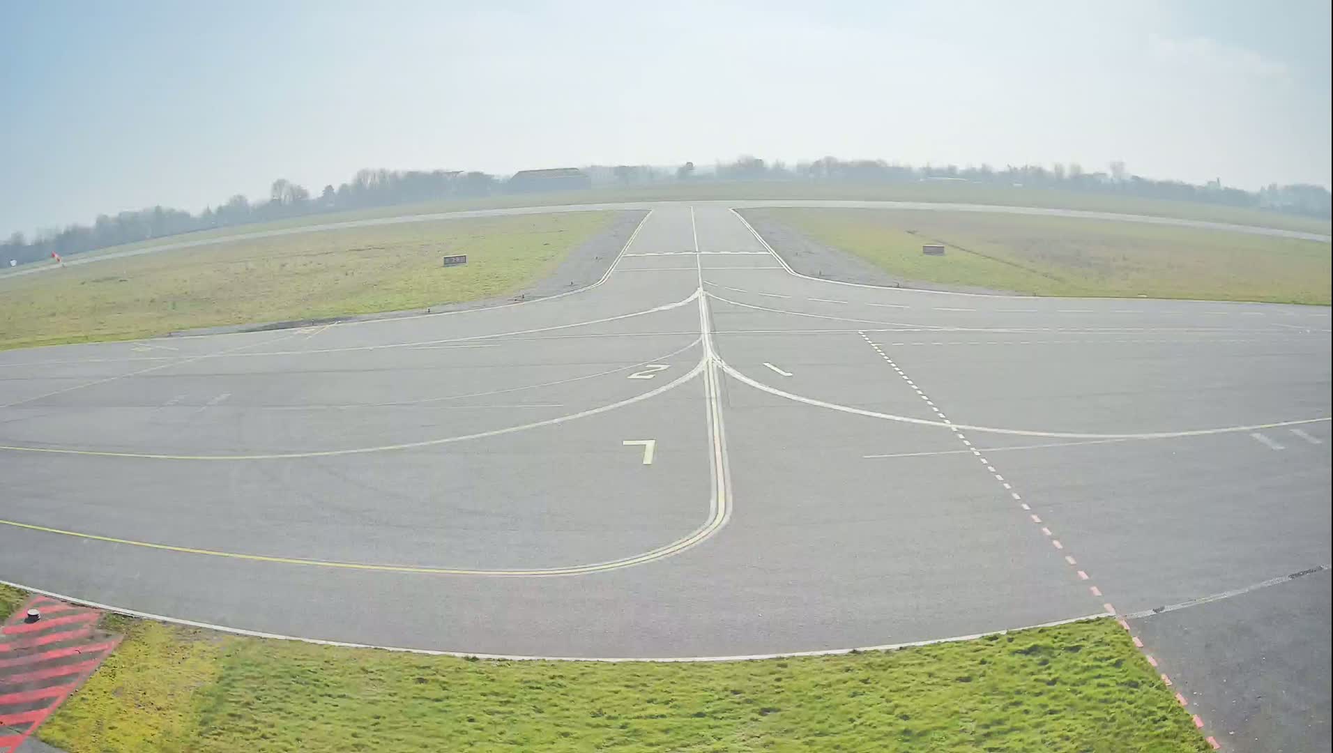 A paved airfield with painted markings under a clear, bright sky is surrounded by short grass.