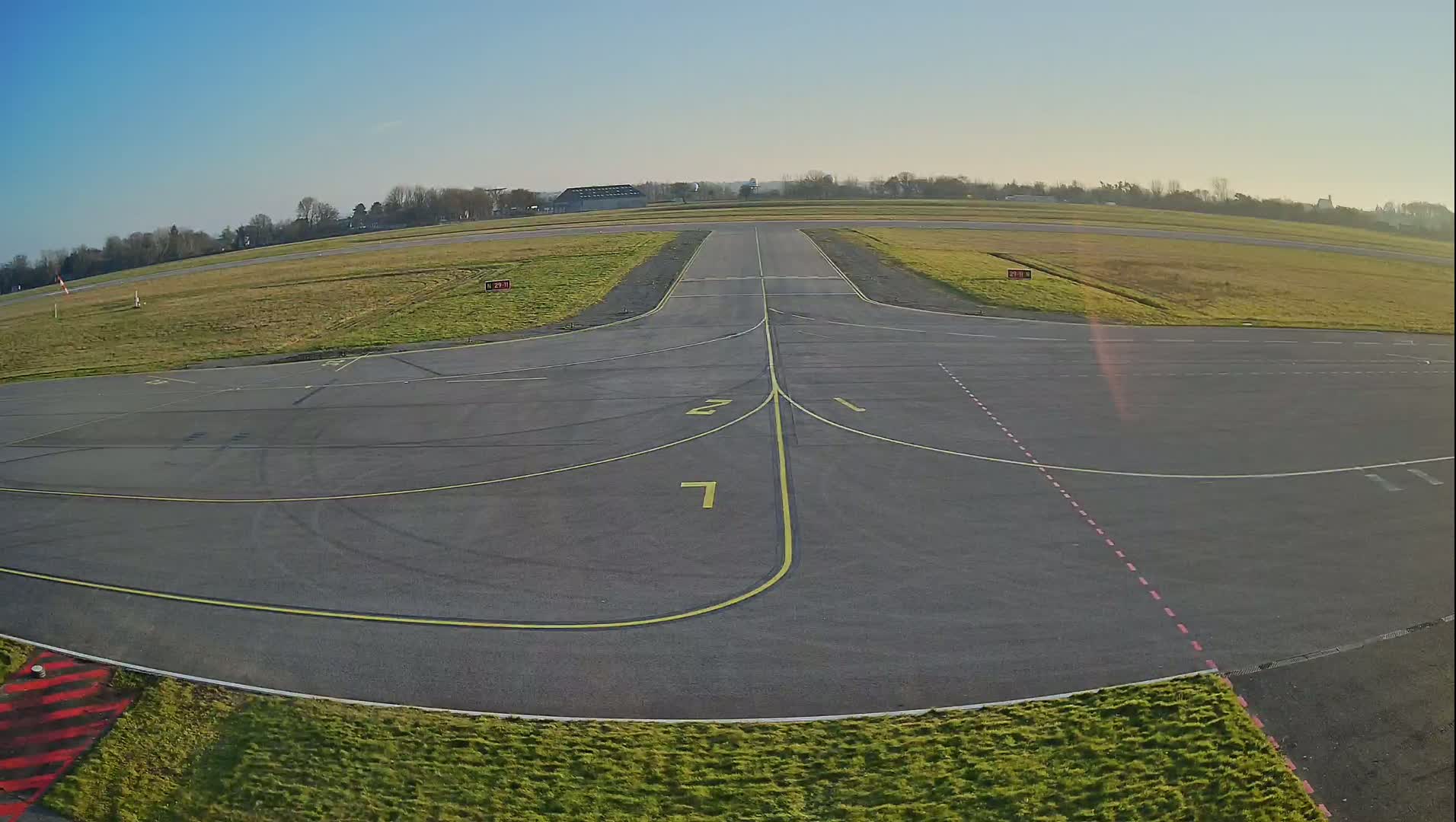 An airfield taxiway with a clear blue sky is seen on a sunny day.