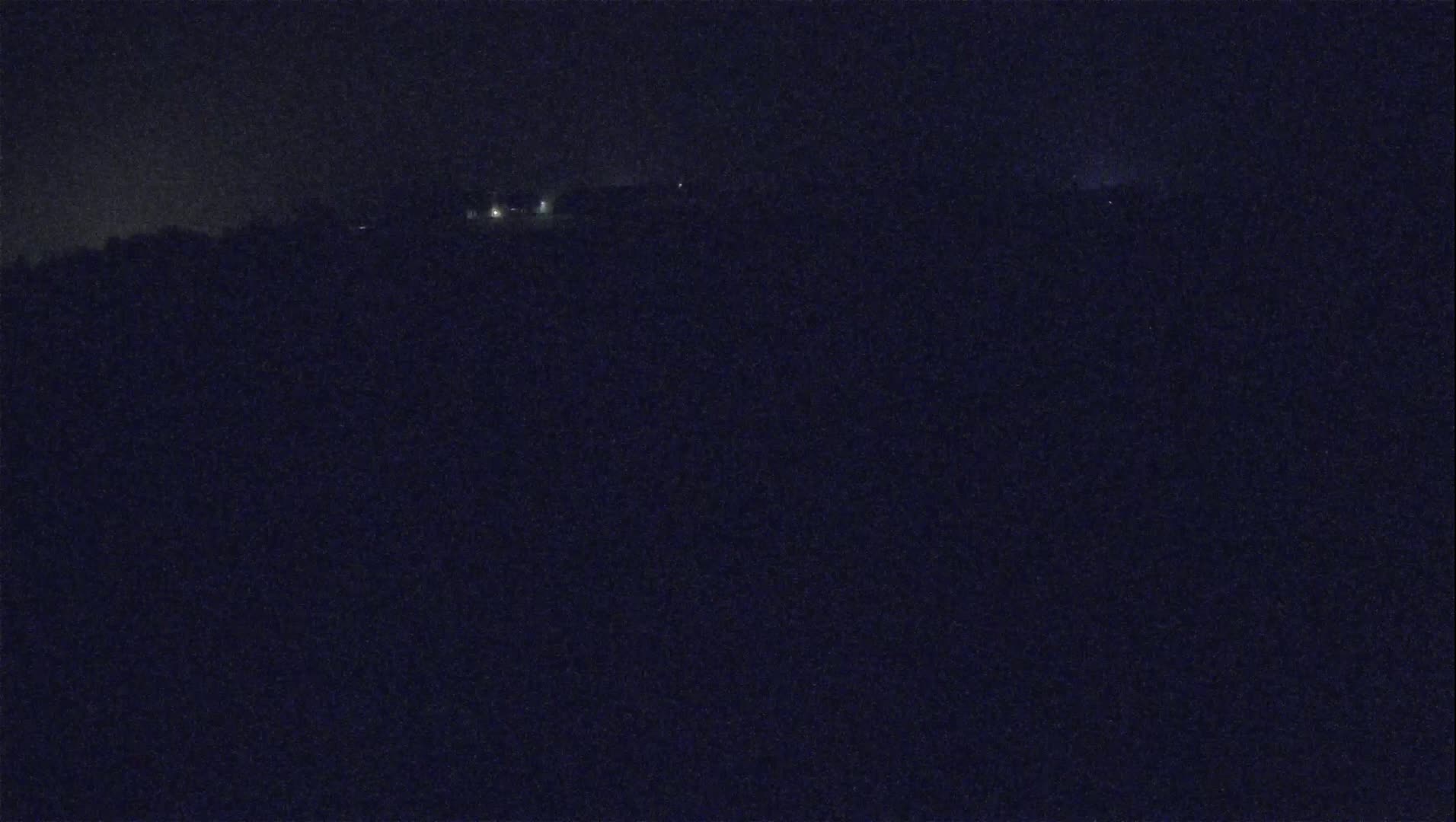 A dark, nighttime view of a distant landscape with a few faint lights visible.