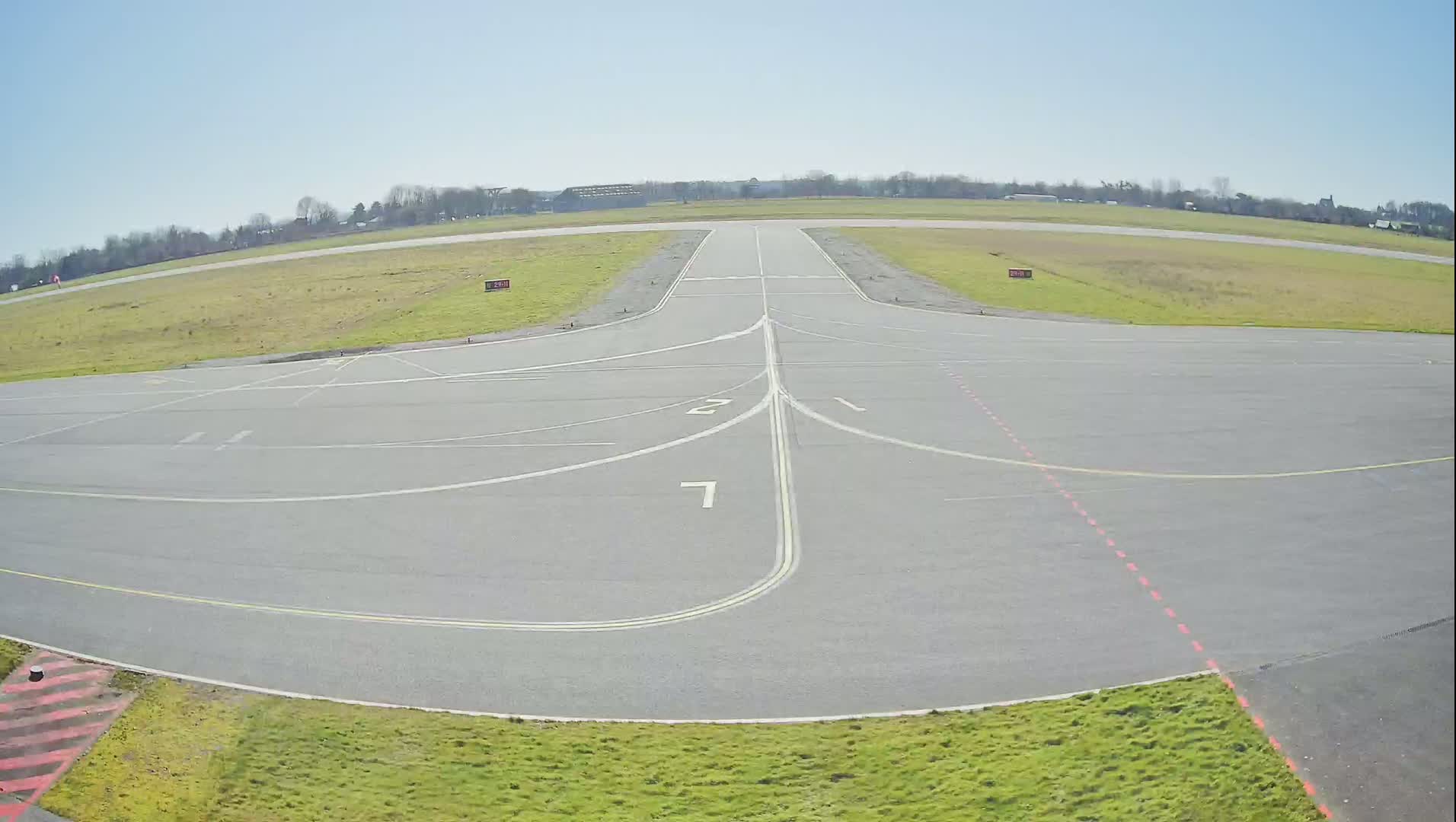 A tarmac airfield with numbered taxiways is visible under a clear, sunny sky.