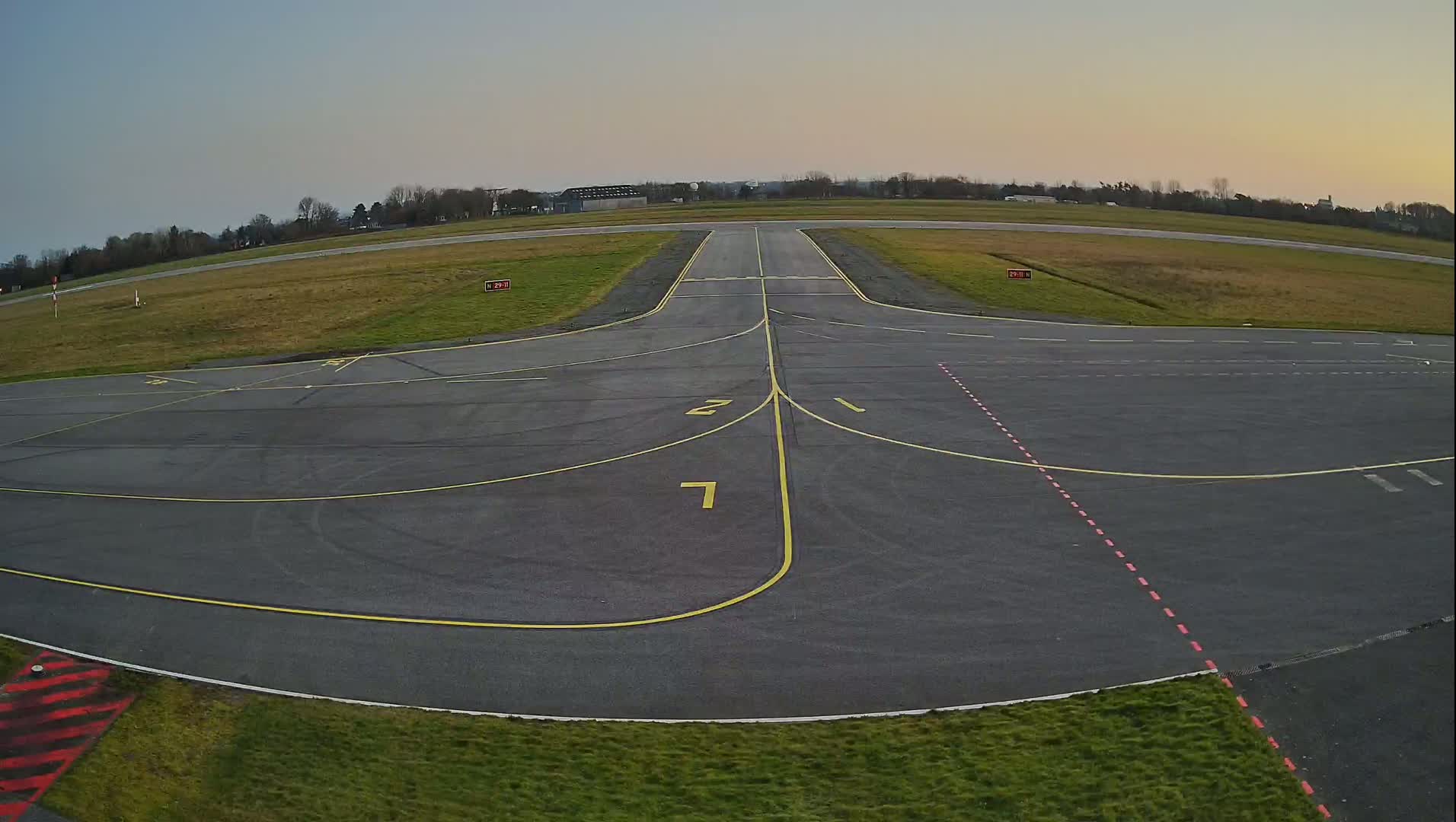 An empty airport tarmac with yellow lines marking taxiways under a clear, twilight sky.