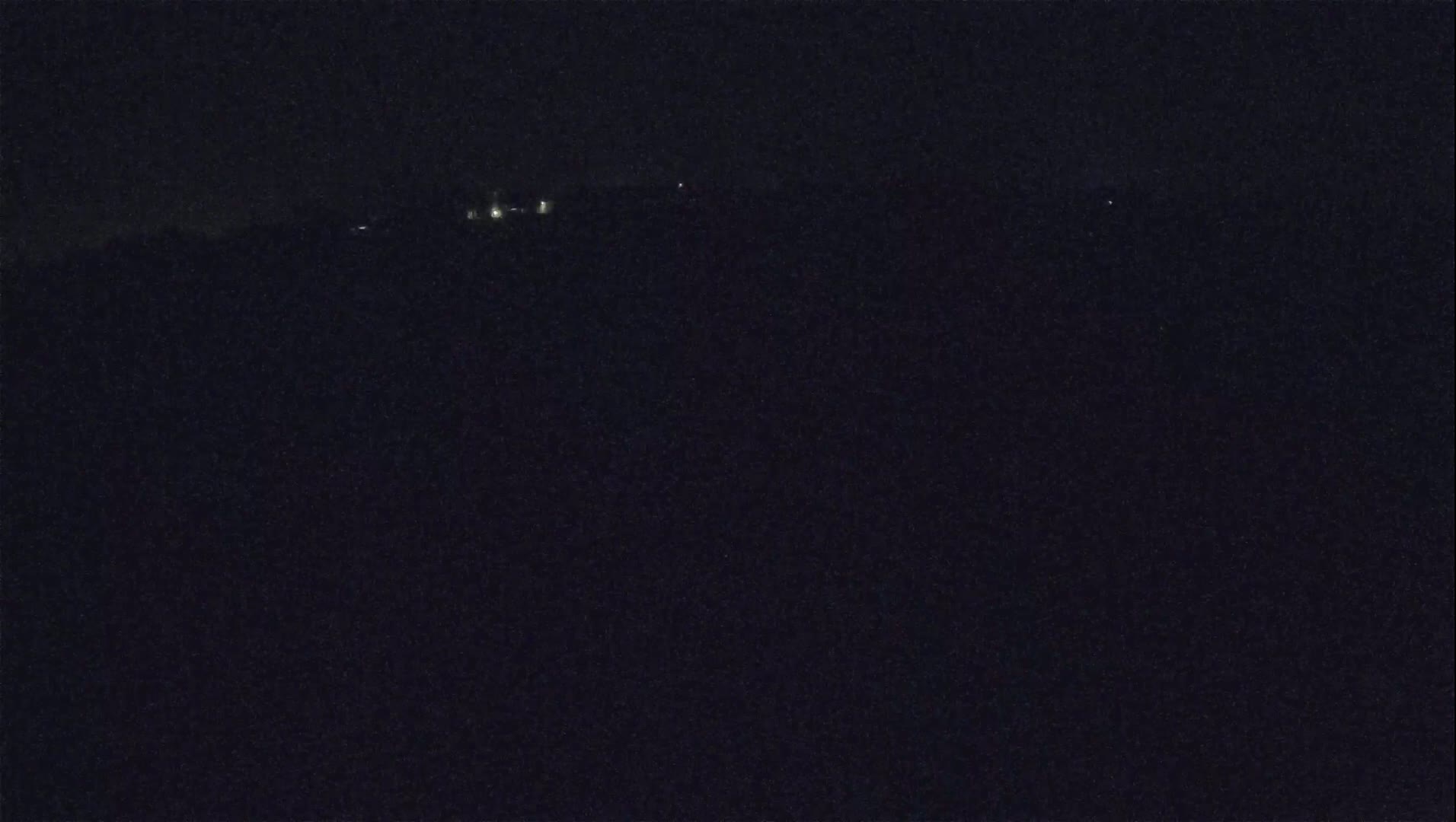 A dark, nighttime landscape shows a few distant lights on a hill.