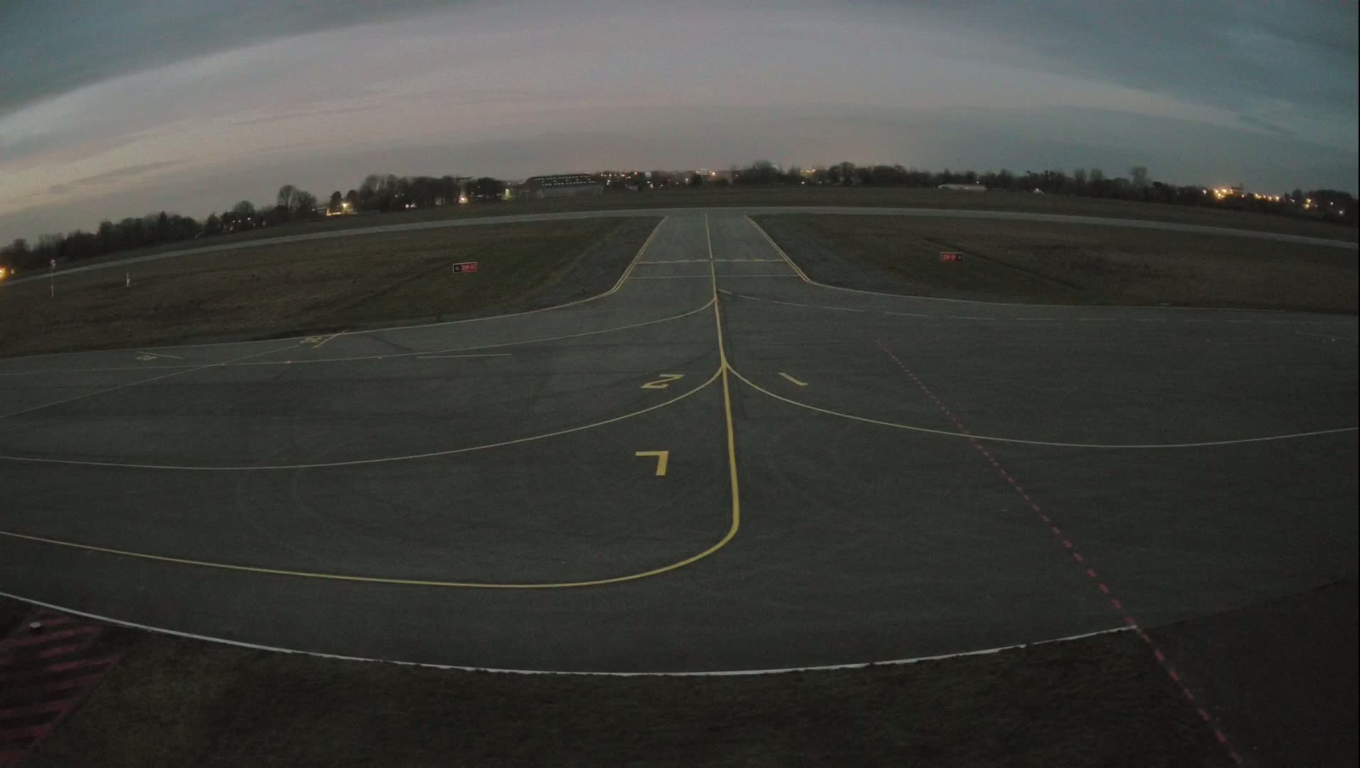 An empty airport runway at dusk under a cloudy sky.