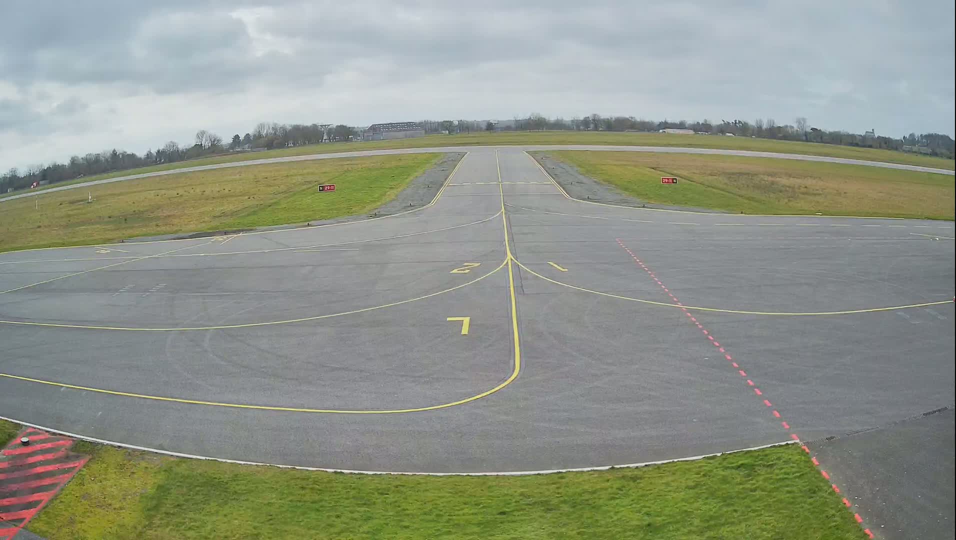 An empty airport tarmac with a runway extending into the overcast sky.