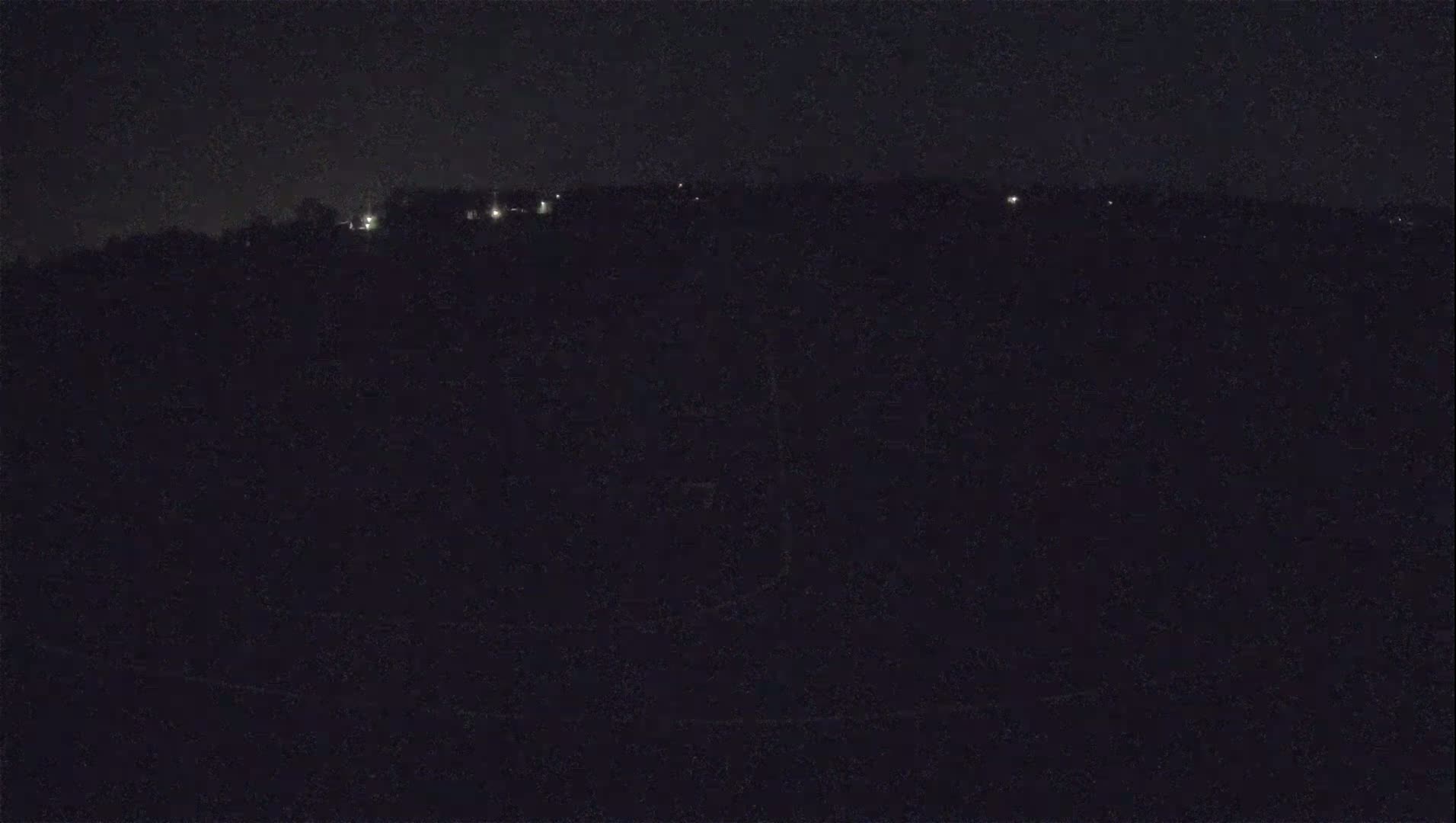 A nighttime, low-light view shows a dark landscape with a few distant lights visible on a hill.