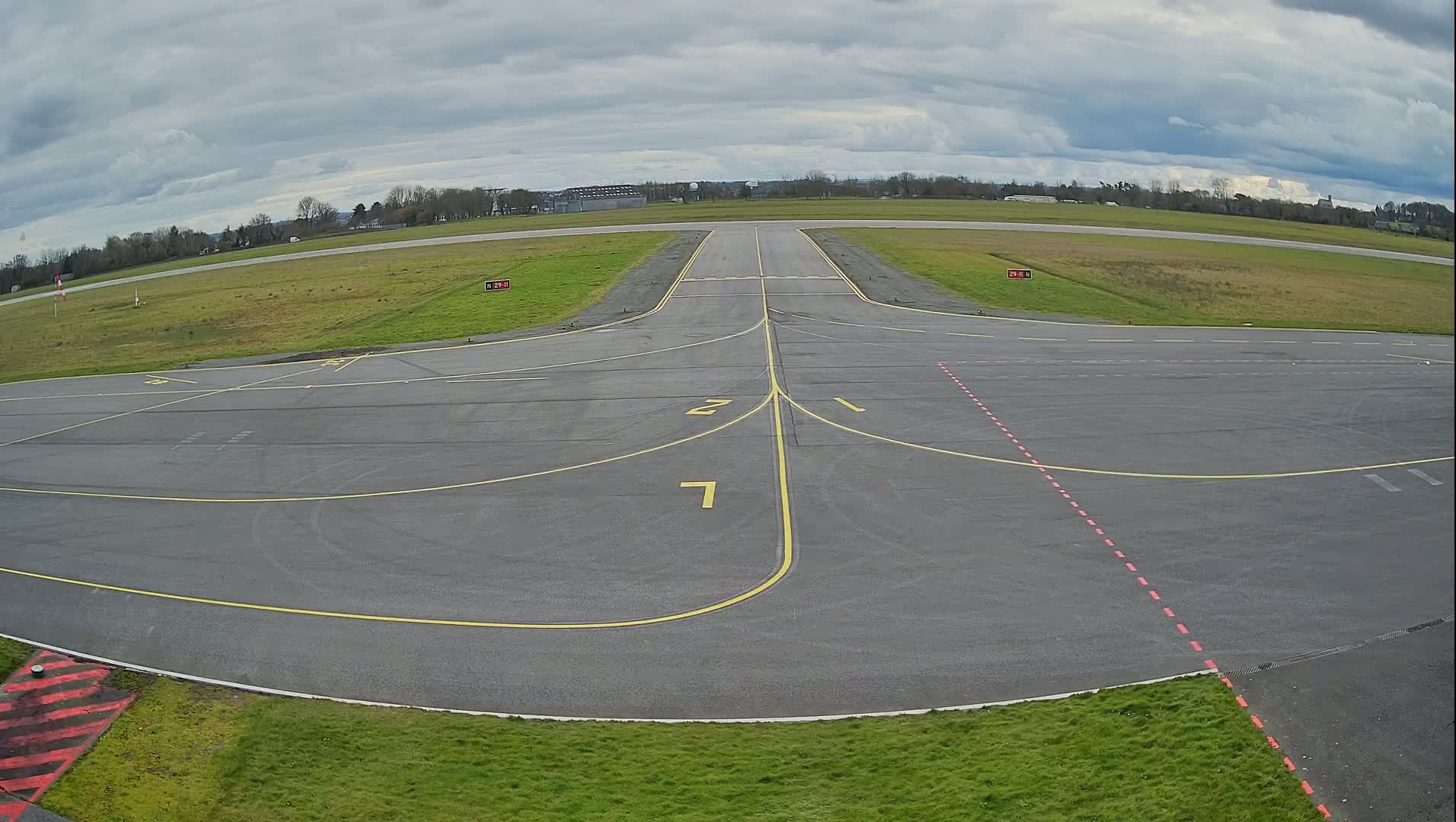 An airfield taxiway with overcast skies is shown in a wide shot.