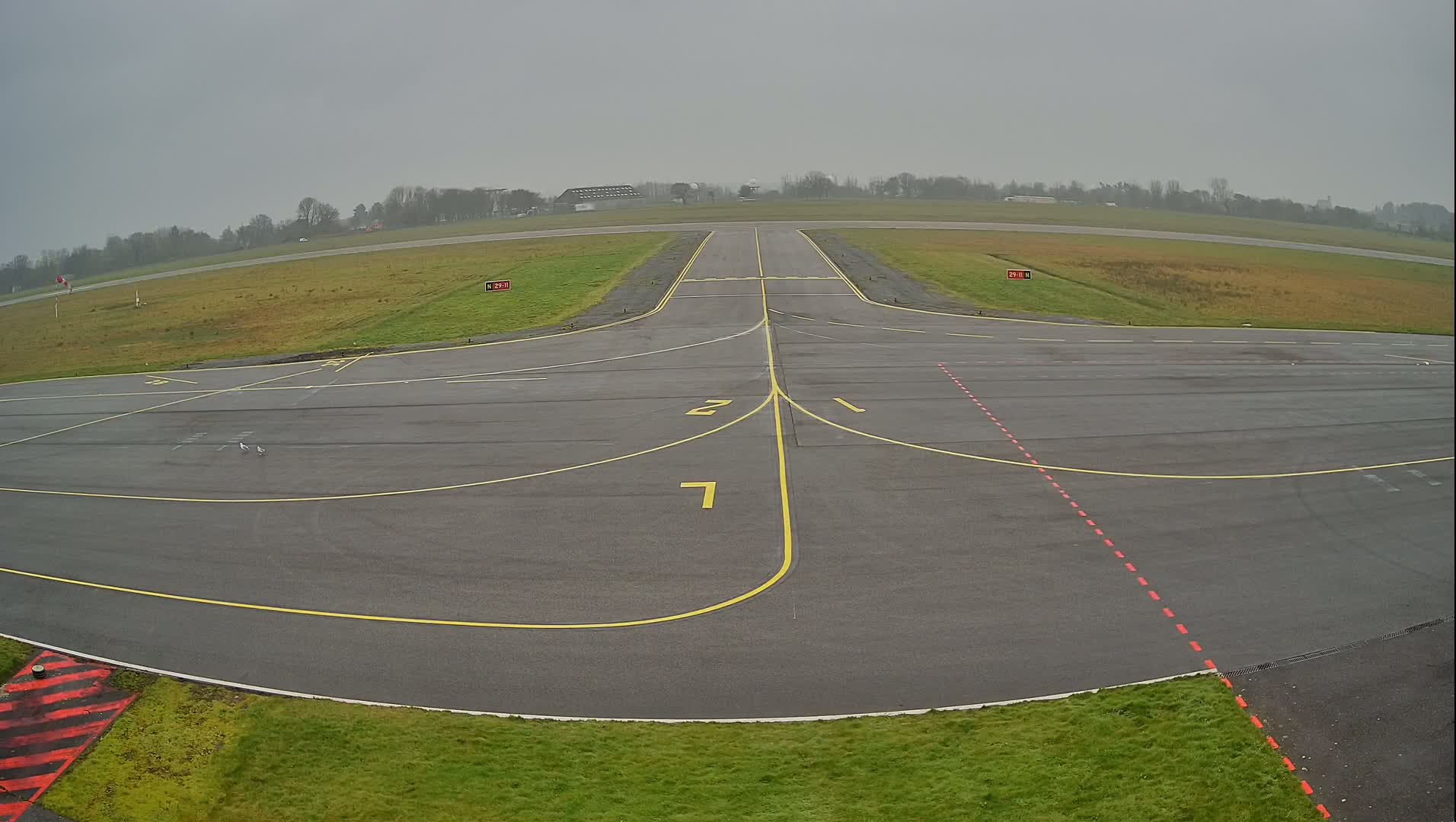 A runway and taxiway at a small airport on an overcast day.