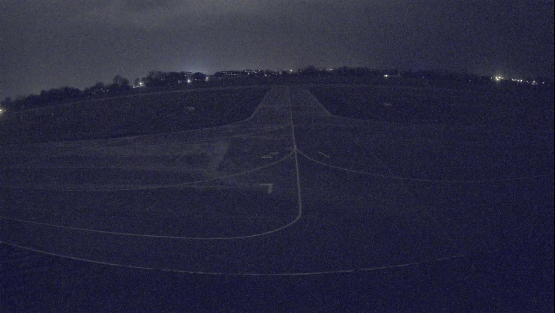 A dark, nighttime view of an airfield runway with faint lighting in the distance.