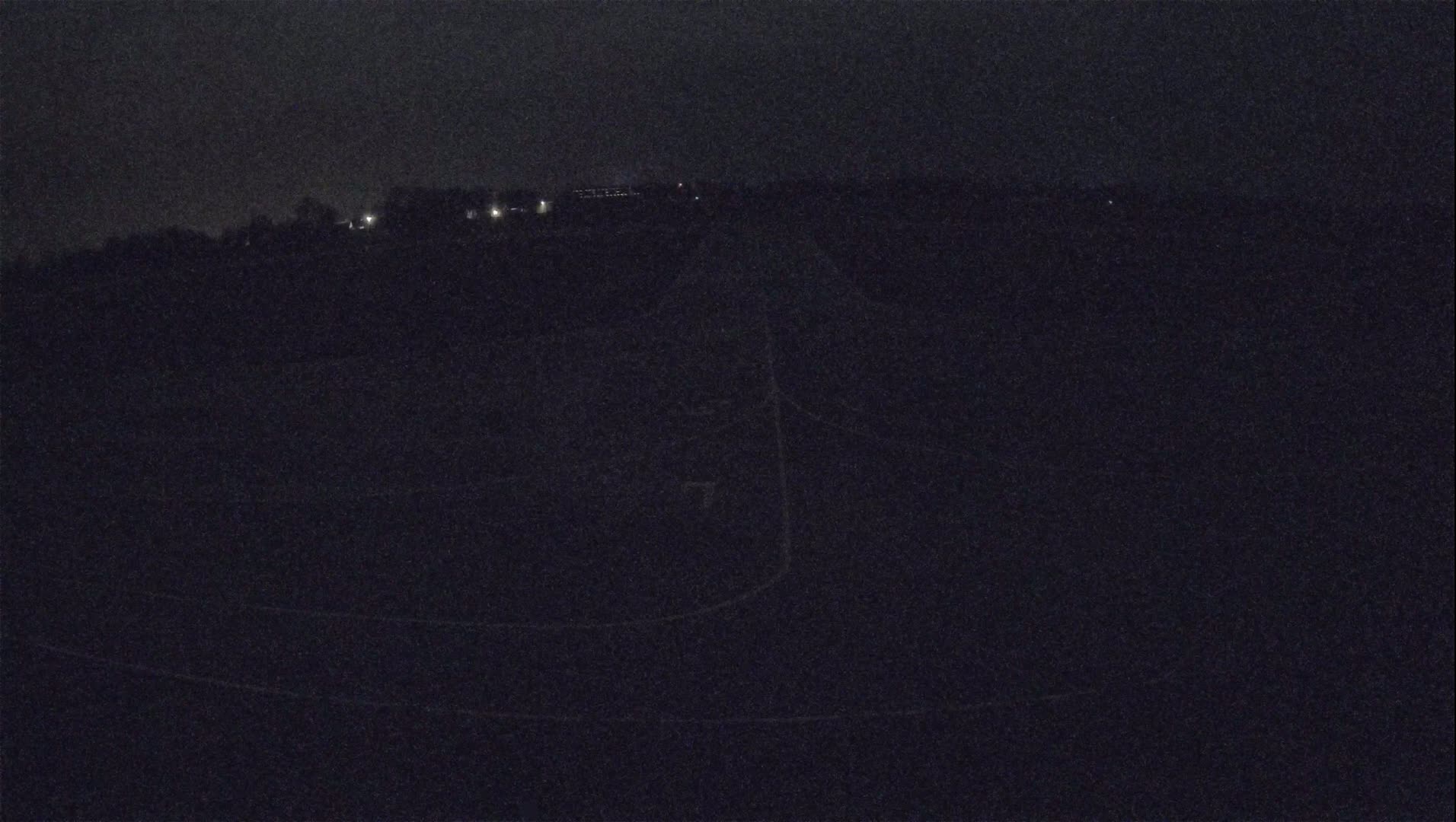 A dark, nighttime scene shows a sparsely lit landscape with a road curving through it.
