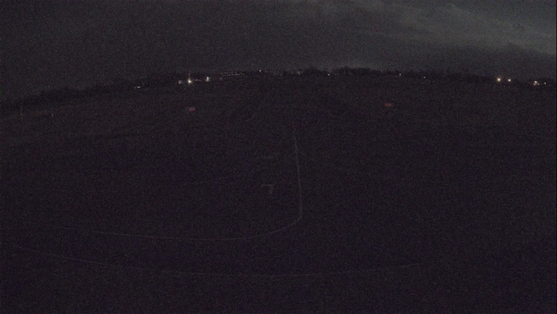 A dark, nighttime view of a flat, sparsely lit landscape under a cloudy sky.