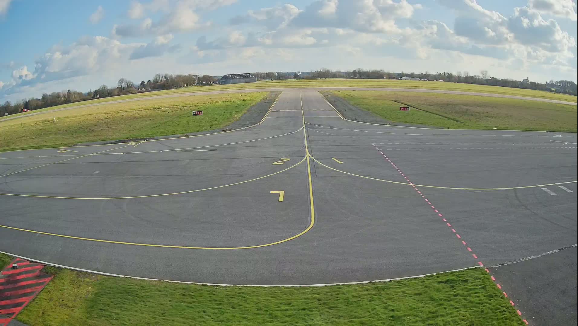 An airfield apron with taxiway markings under a partly cloudy sky.