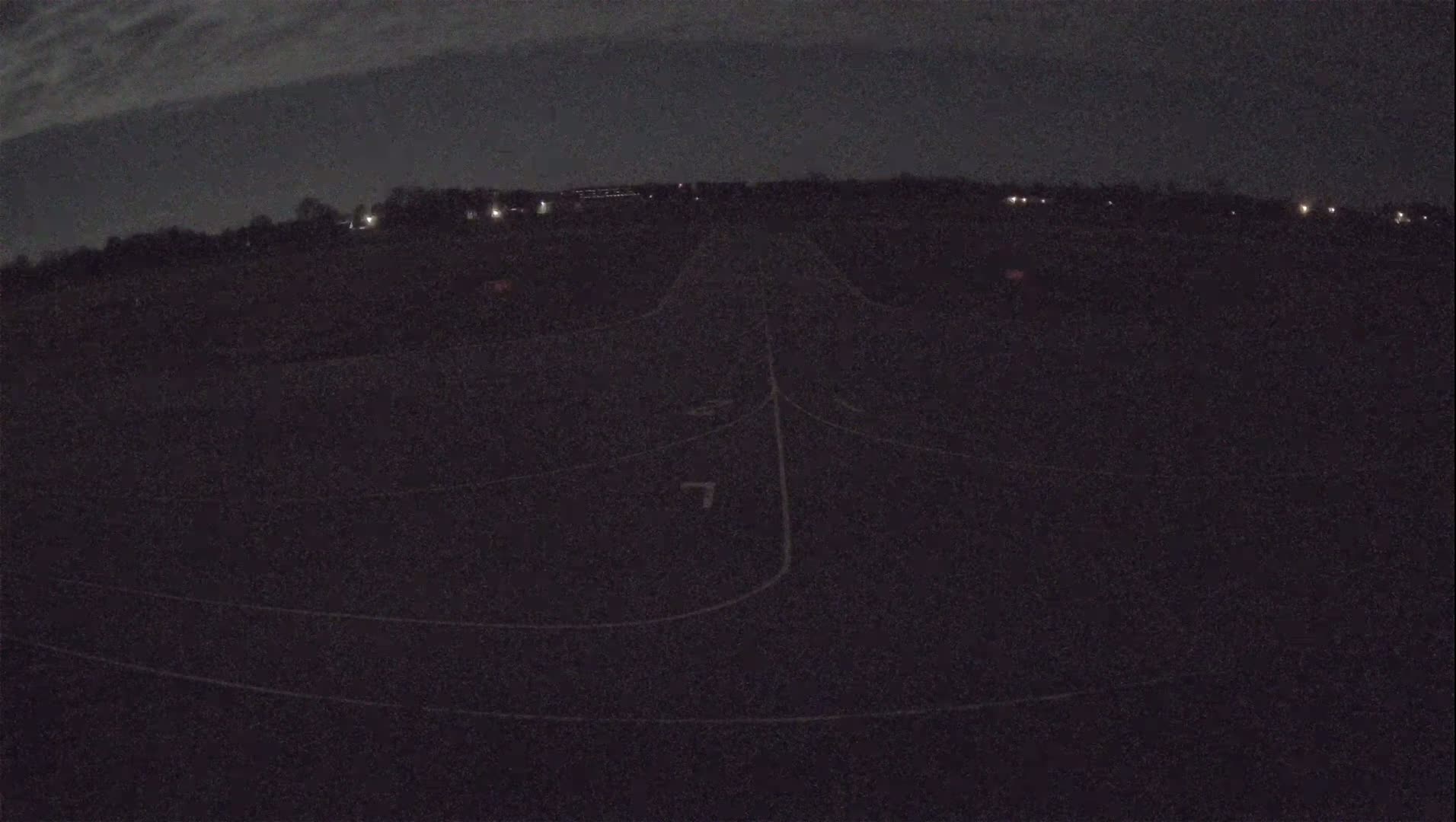 A dark asphalt surface with faint white markings, possibly a runway or racetrack, is visible under a nighttime sky with a few clouds.