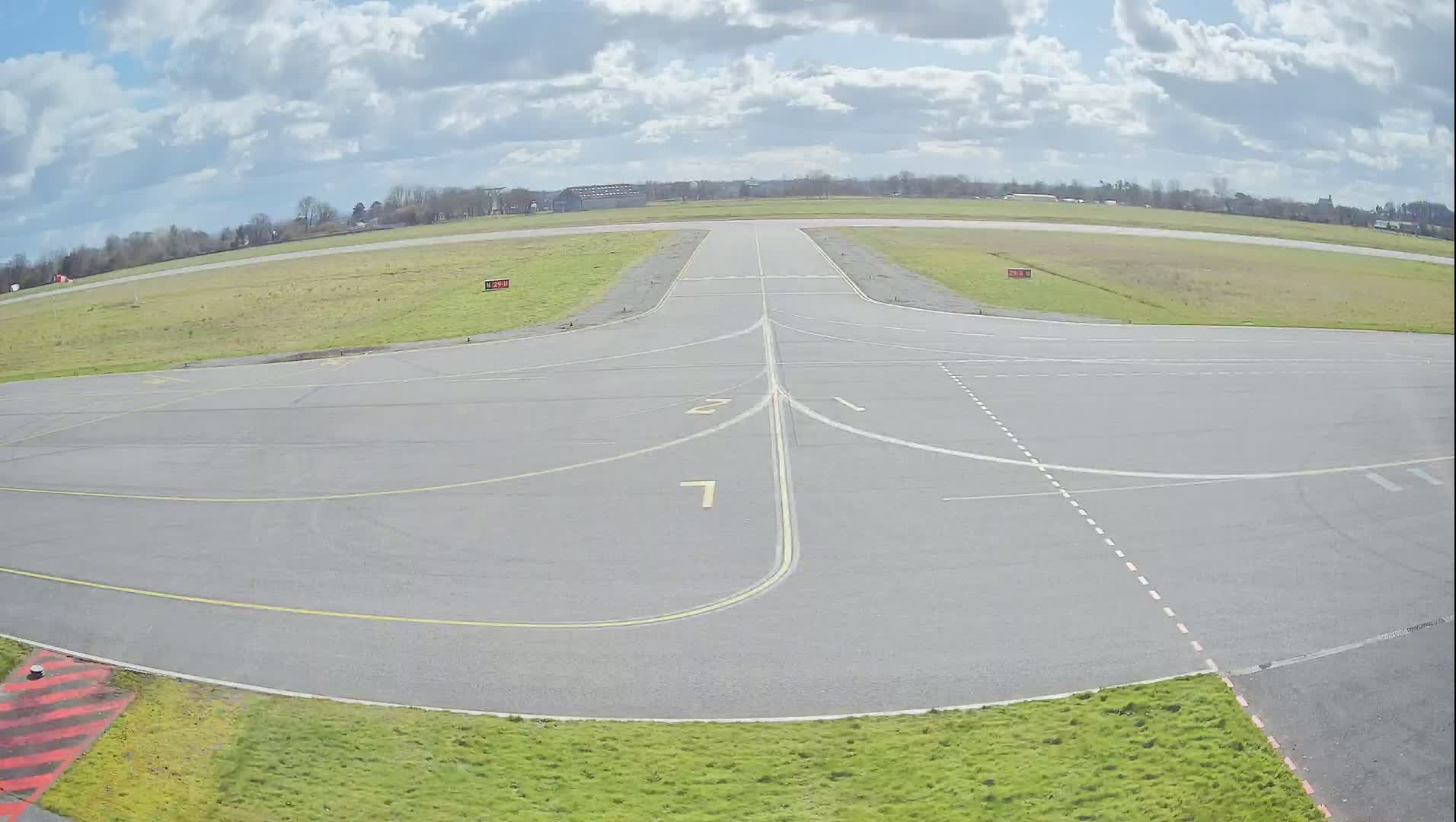 A paved airport runway with numbers painted on it is surrounded by grassy areas under a partly cloudy sky.