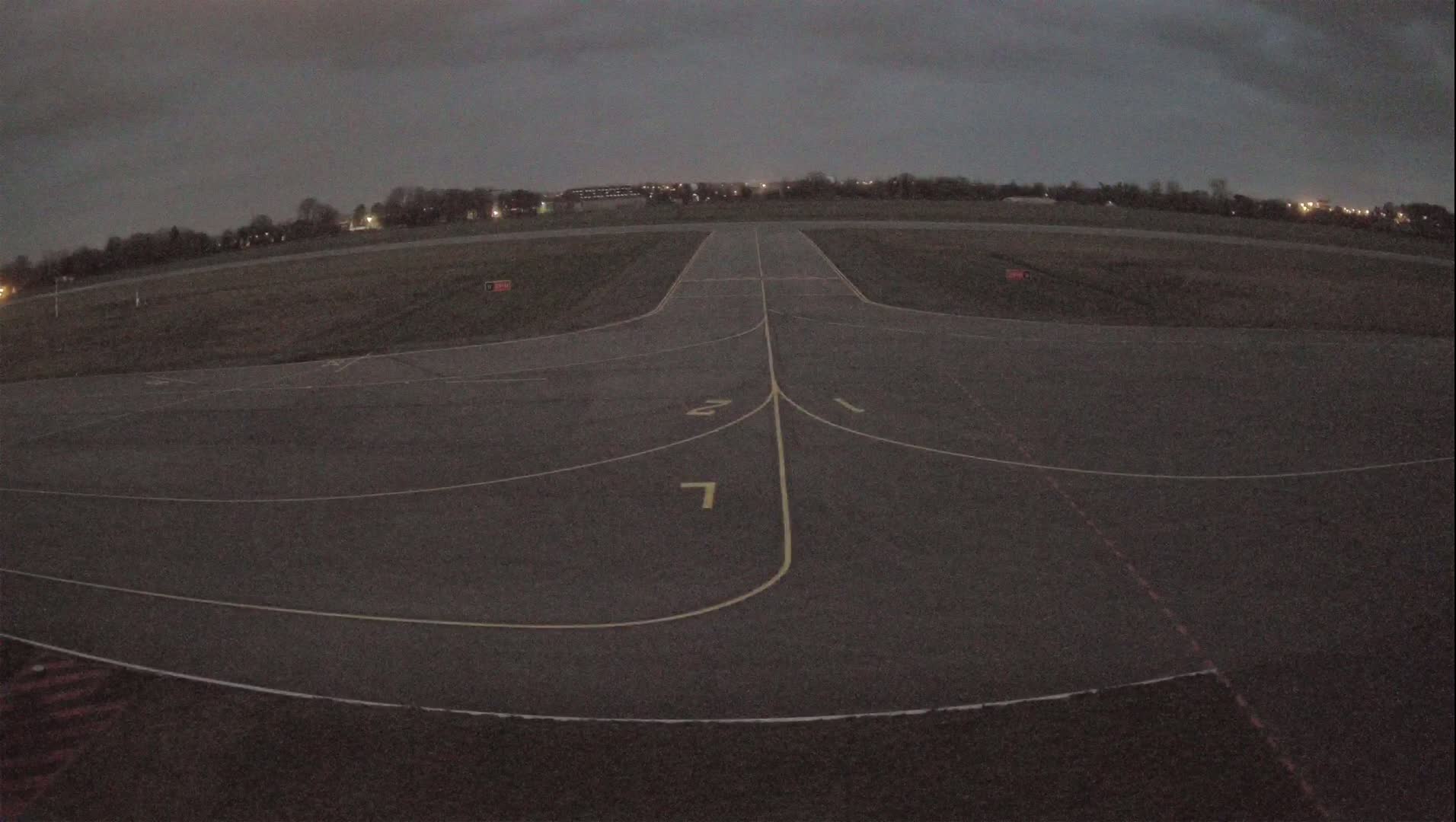A dark, overcast sky hangs over an empty airport runway with painted lines and numbers.
