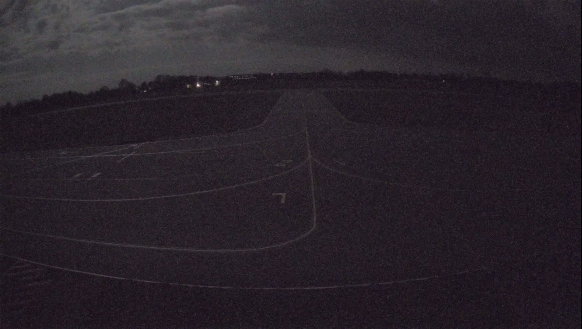 A dark, nighttime view of a paved area with white lines marking lanes, under a cloudy sky.