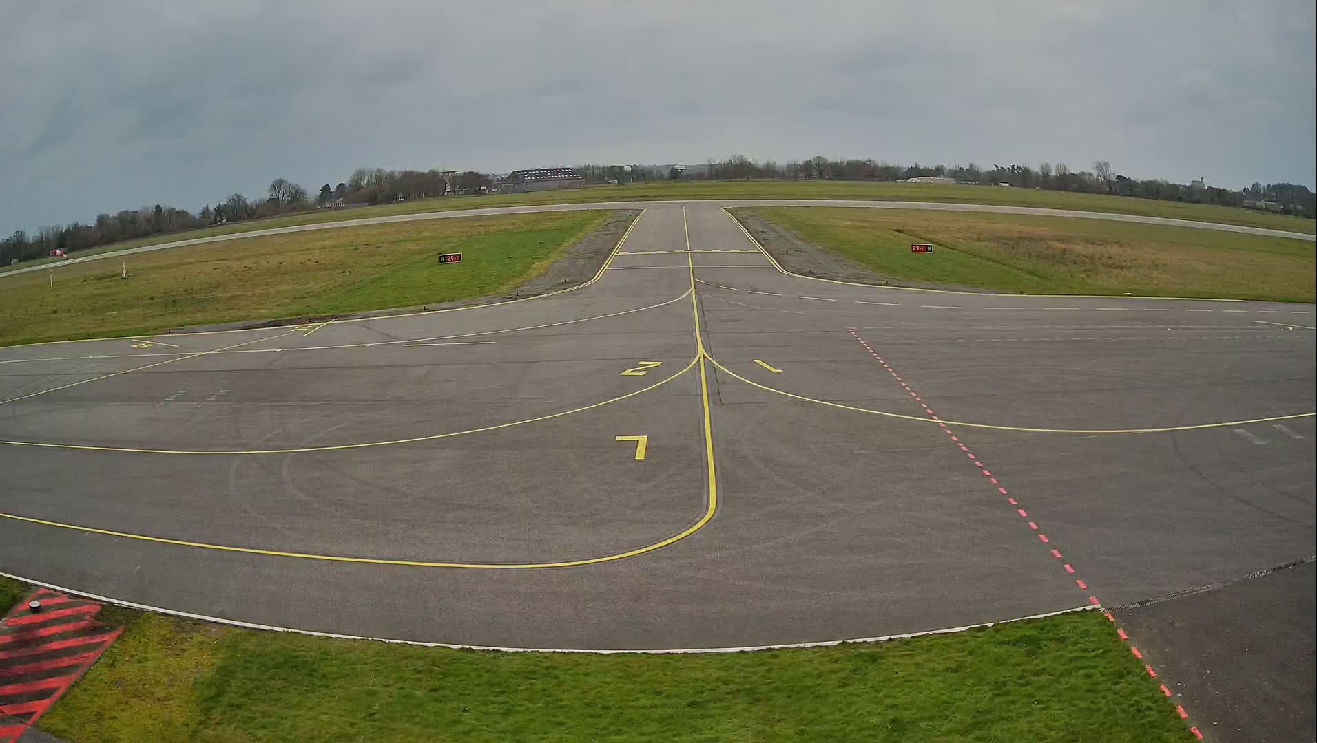 A tarmac area of an airport with yellow and red markings is shown under an overcast sky.