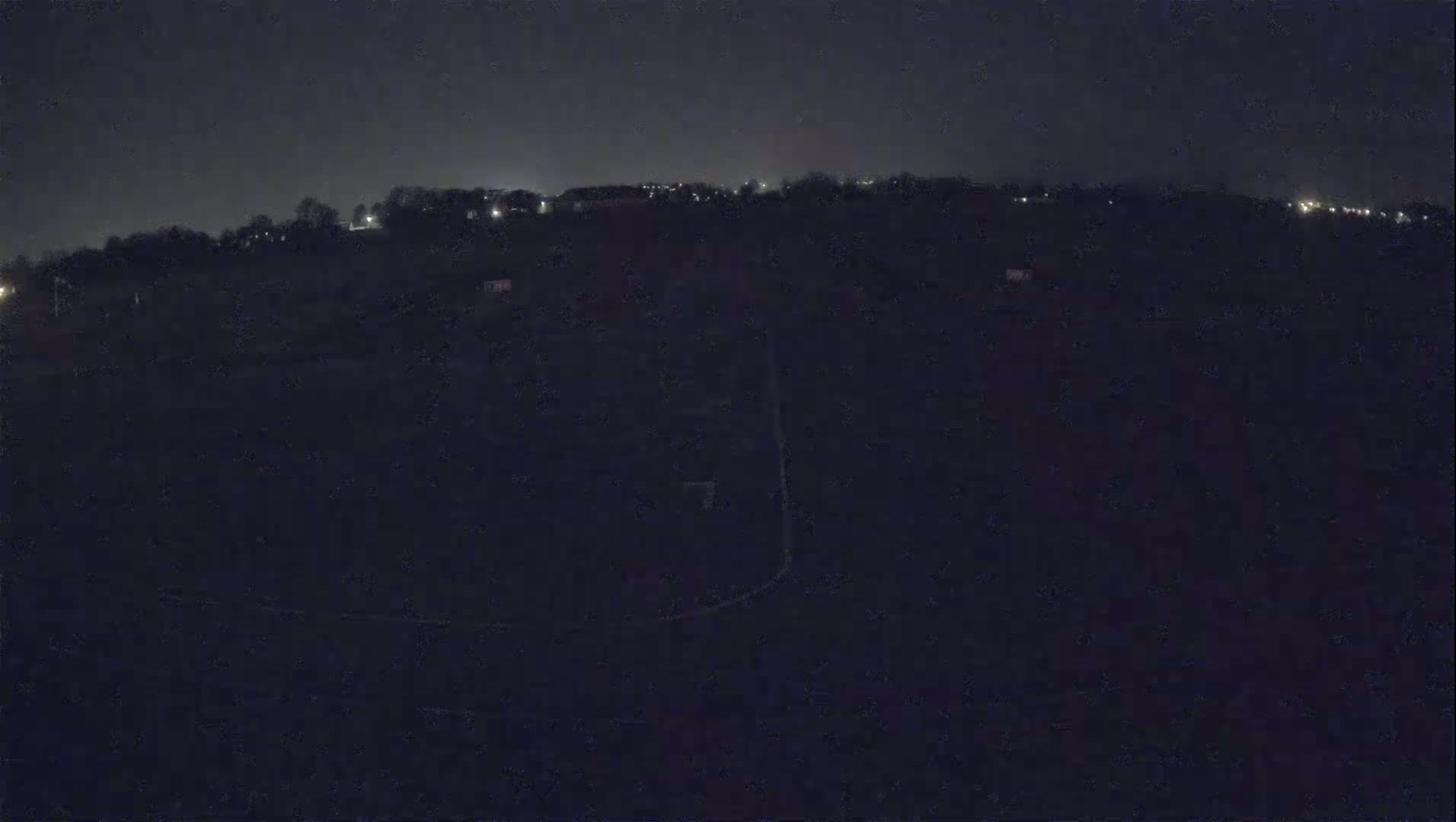 A dark, nighttime view of a mostly obscured landscape with a few distant lights visible on a hill.