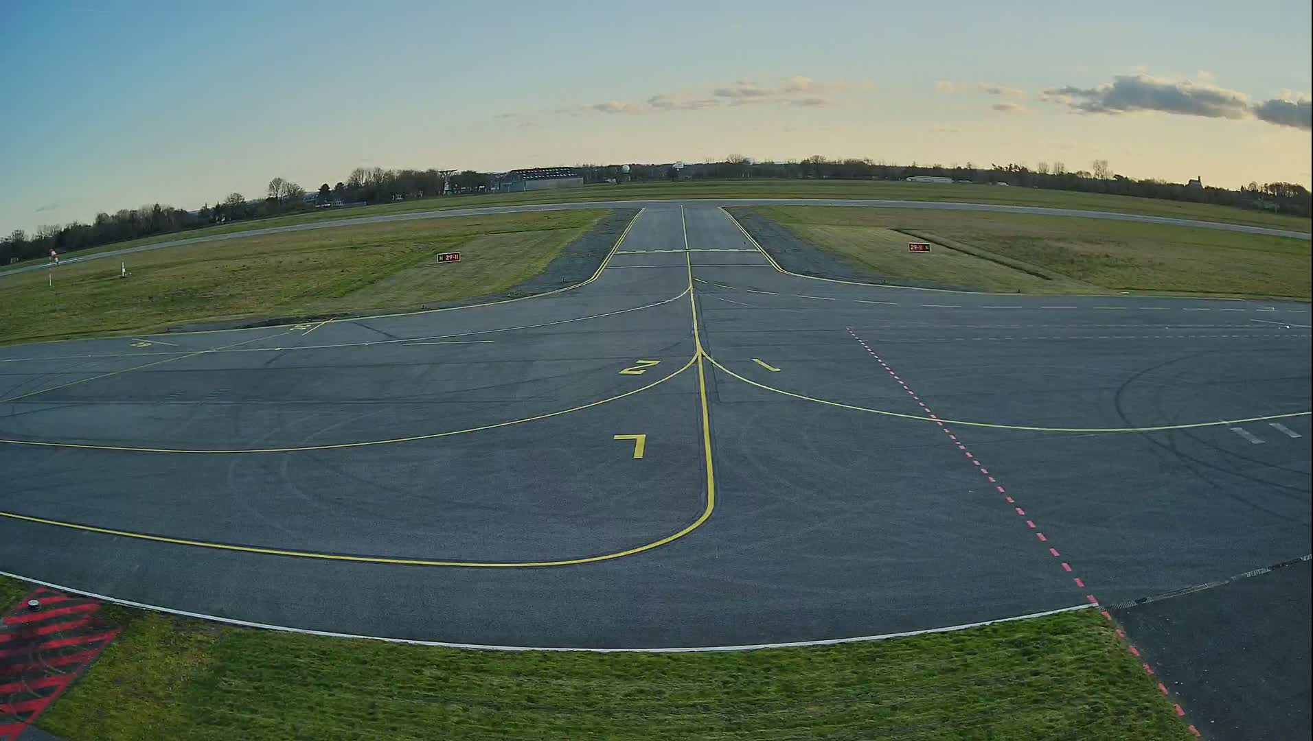 An airfield's tarmac runway and taxiways are visible under a mostly clear sky, with some clouds.