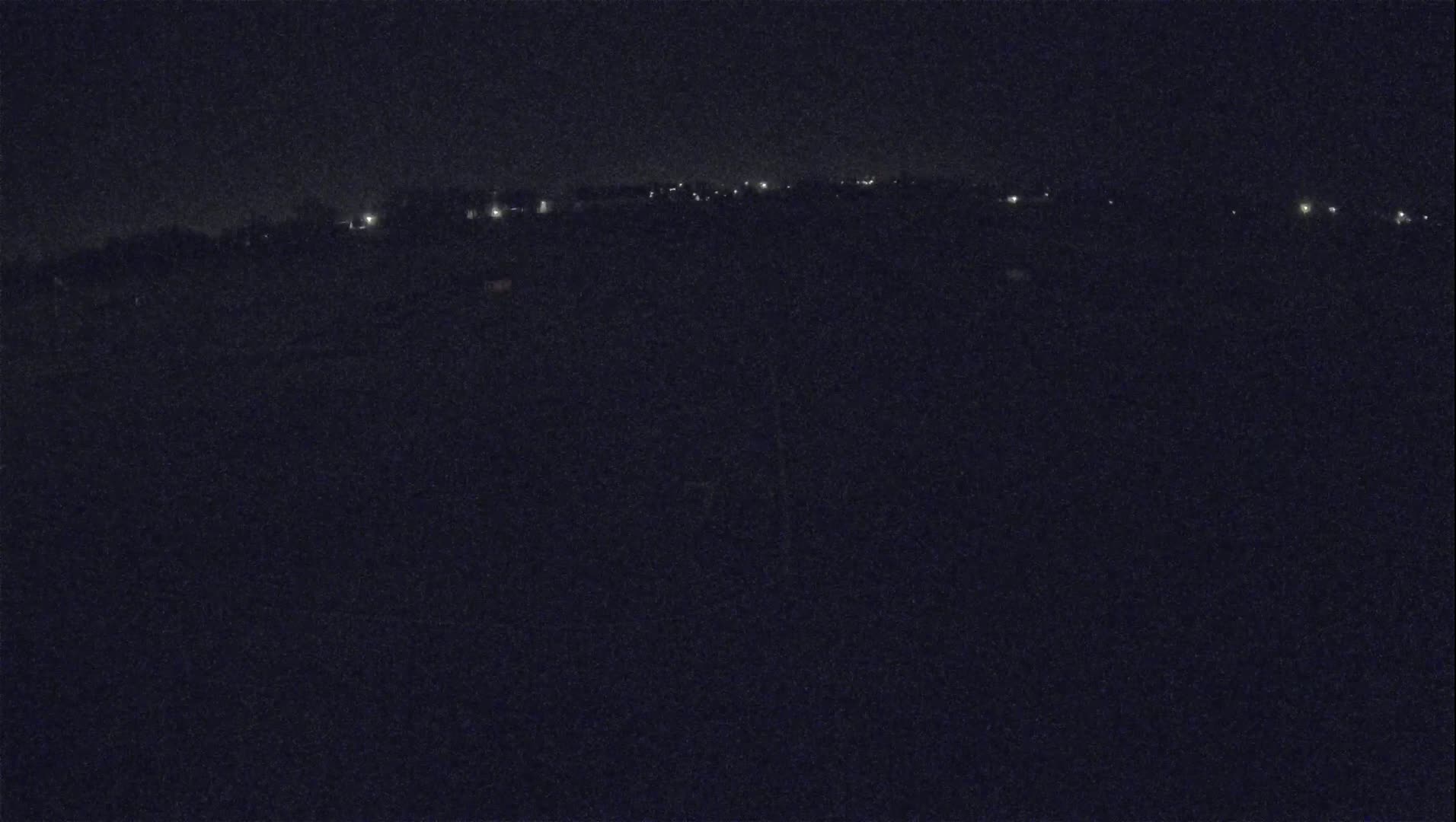 A nighttime, low-light view of a dark landscape with a distant line of faint lights.