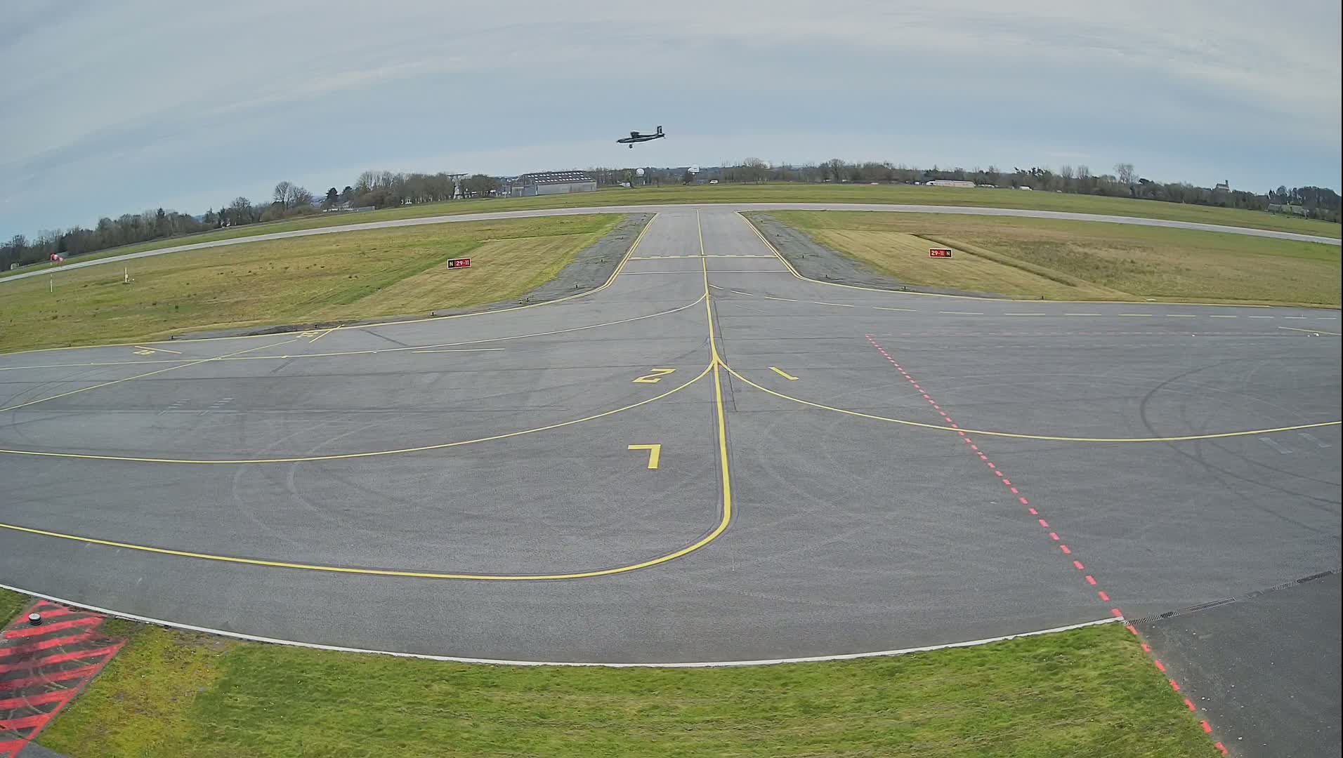 A small airplane is seen flying over a tarmac runway on an overcast day.