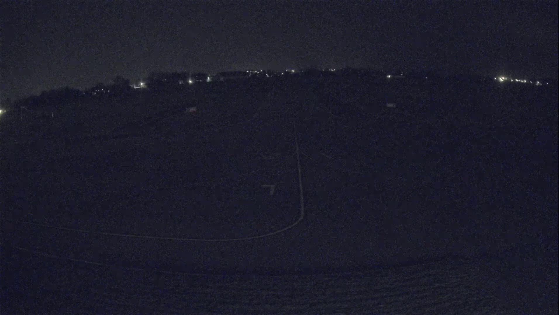 A nighttime, low-light view of a dark field with faint outlines of a track and distant lights.