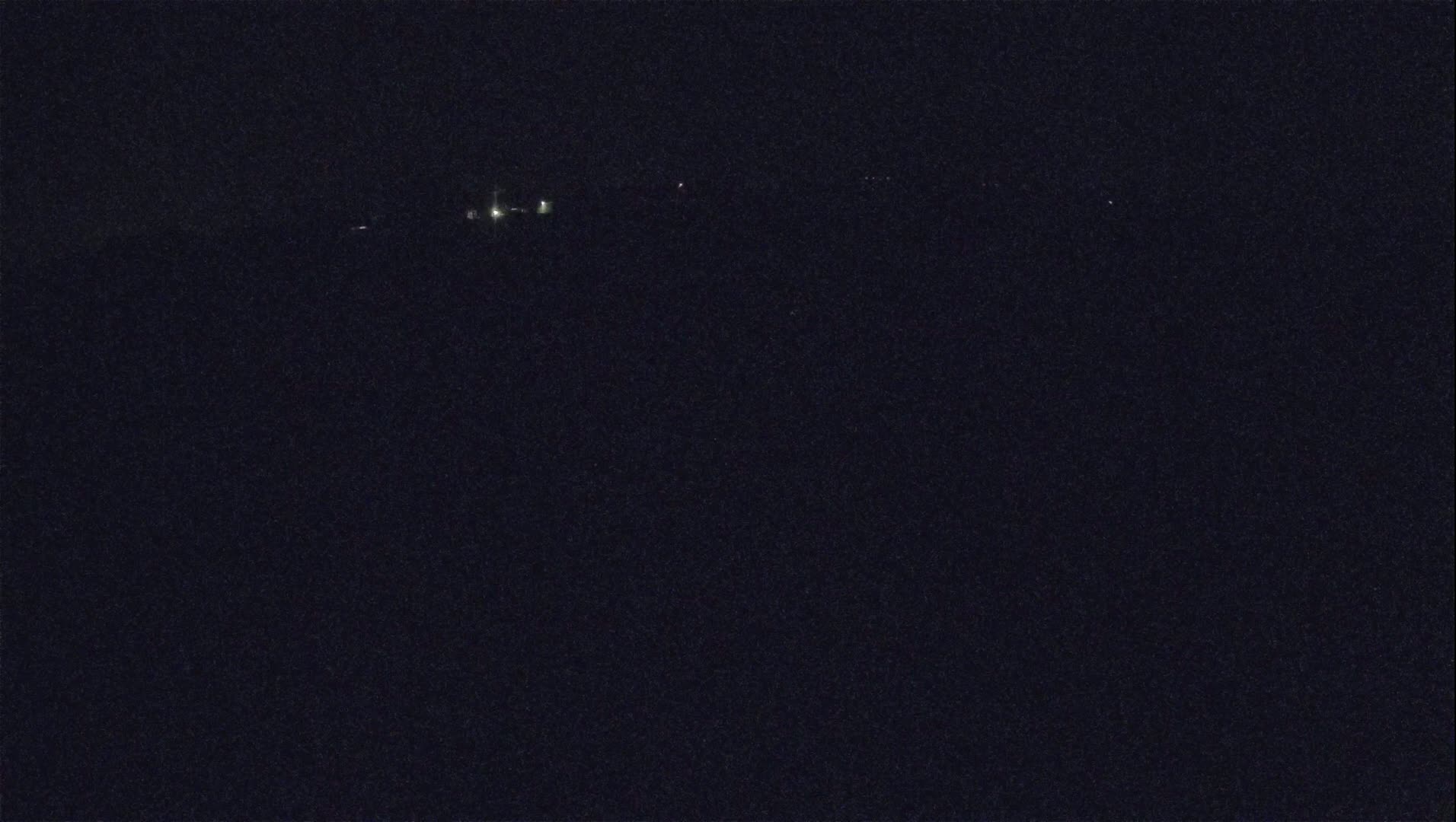 A dark, nighttime scene shows a few distant, faint lights on the horizon.